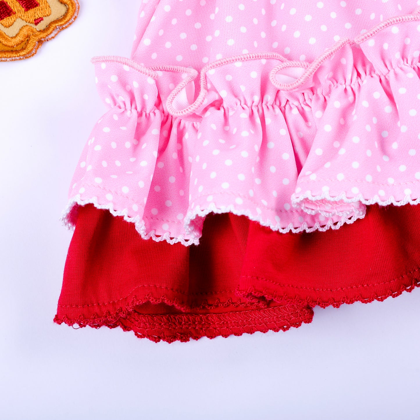 Close-up of pink polka dot and red layered ruffled hem trim on girls boutique embroidered top.
