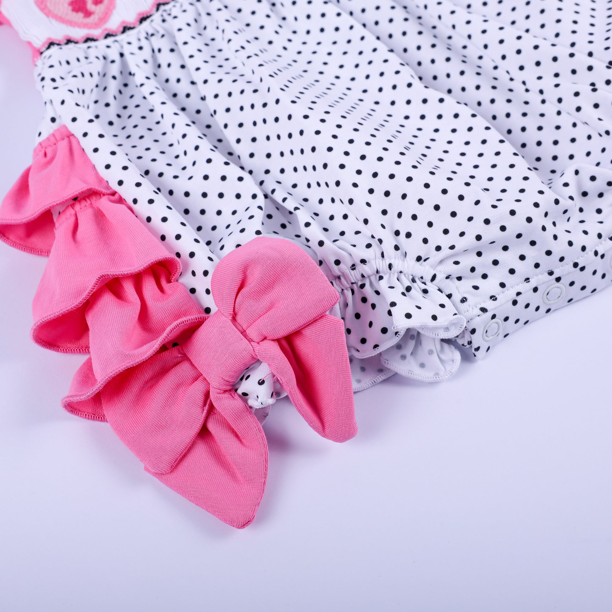 Close-up view of pink side ruffle accent and bow detail on polka dot hand-smocked baby girl bubble romper bottom.