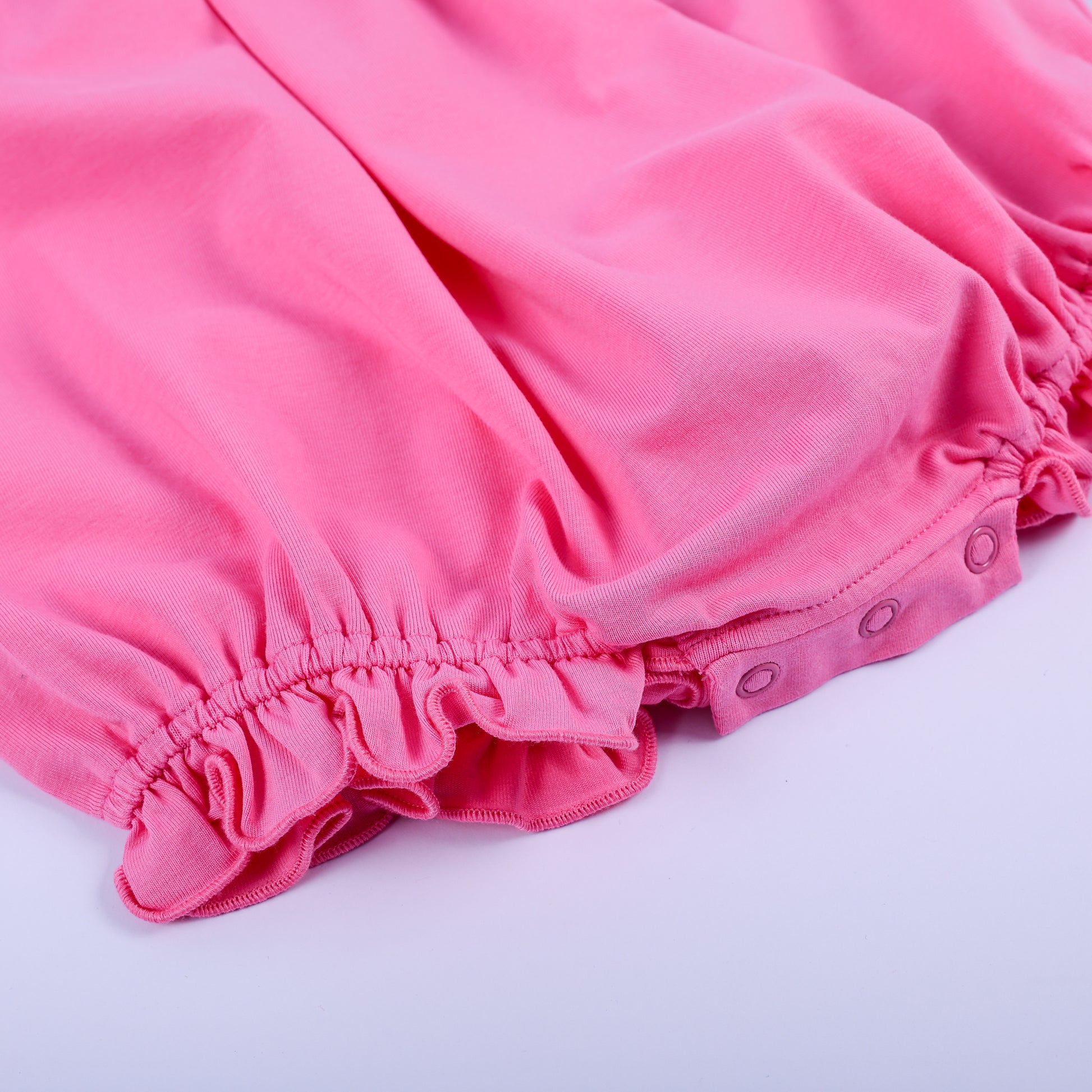 Close-up of ruffled leg openings and convenient snap closure on a pink hand-smocked knit bubble romper for infants.