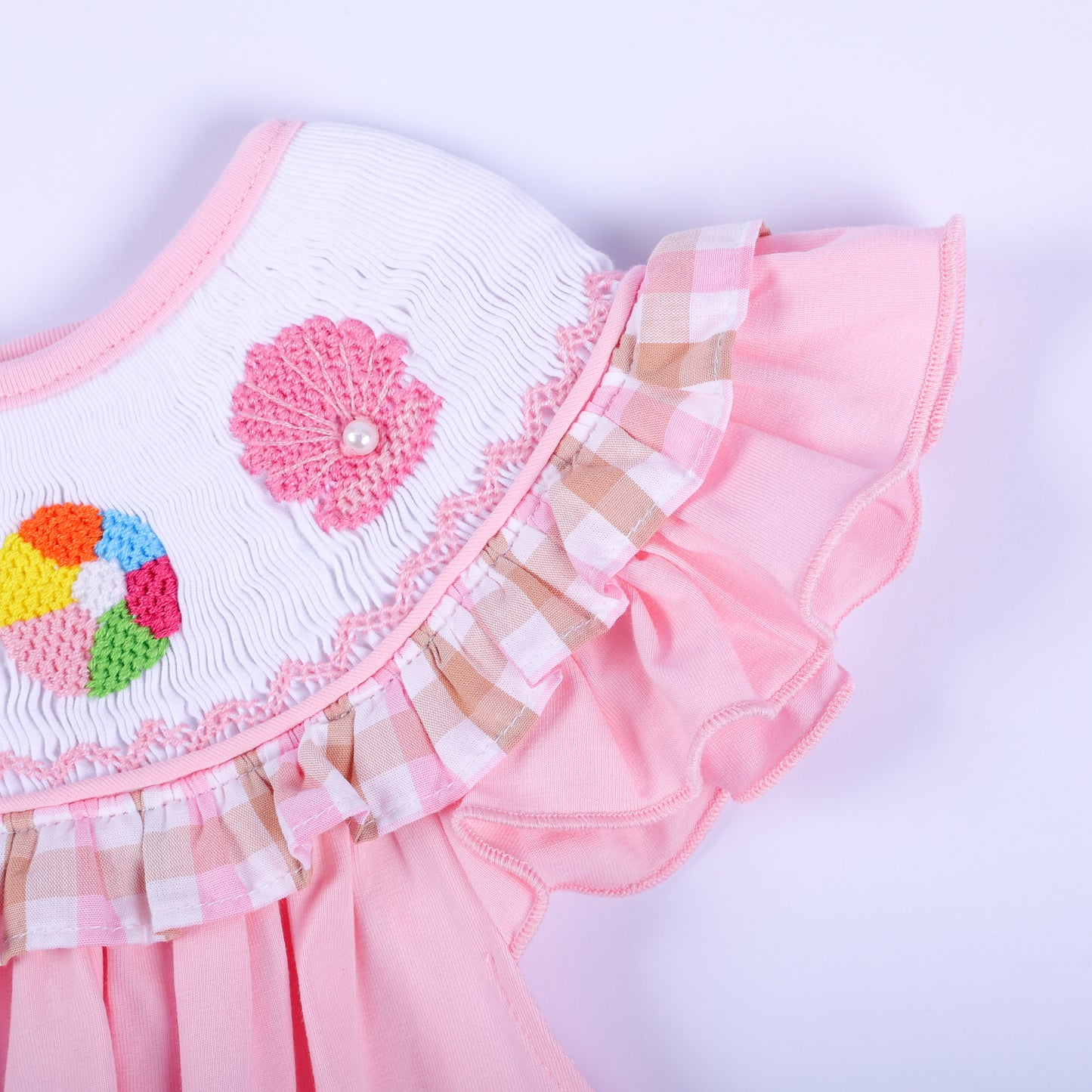 Detailed view of pink gingham ruffle sleeve and hand embroidered pink seashell on a girl's smocked beach dress.