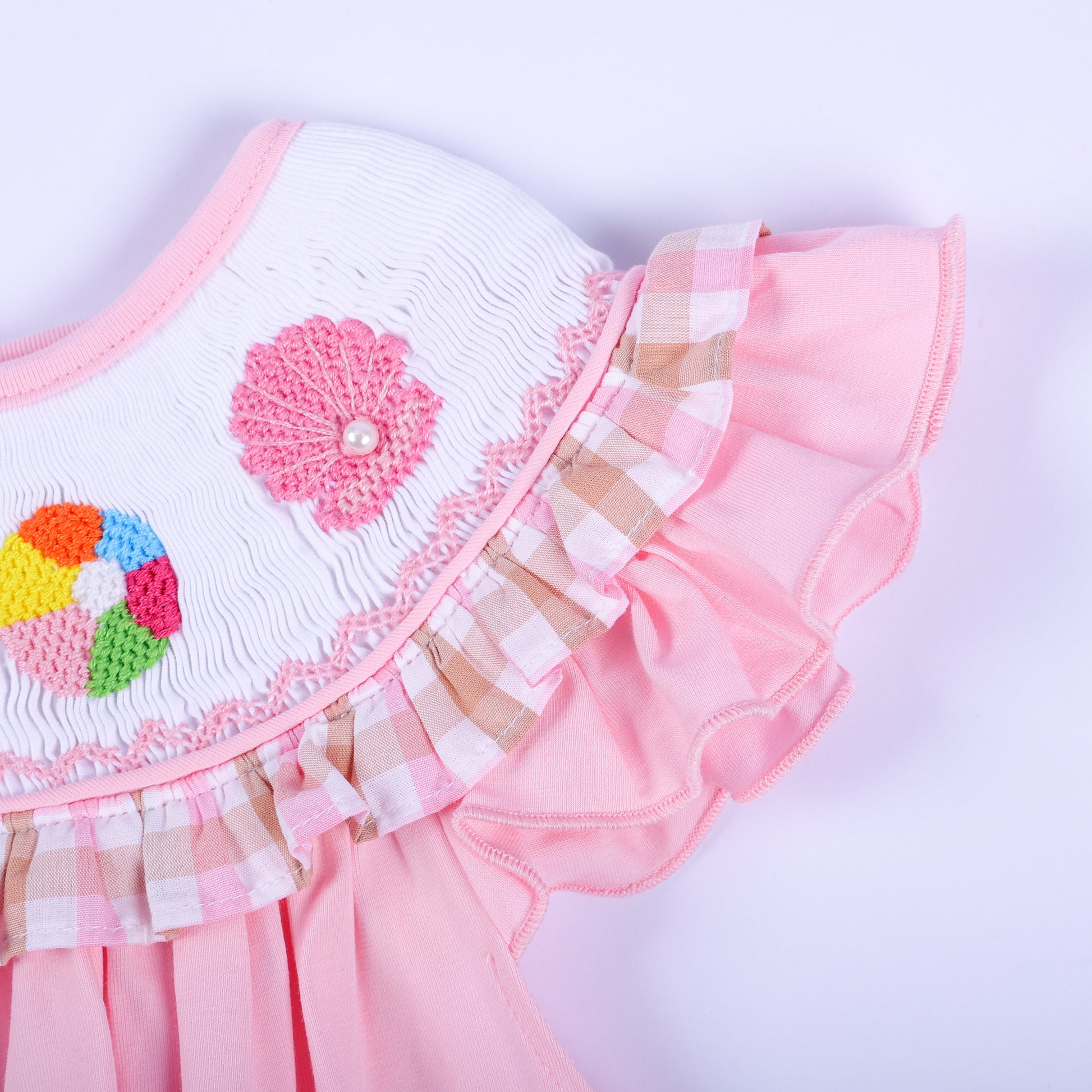 Detailed view of pink gingham ruffle sleeve and hand embroidered pink seashell on a girl's smocked beach dress.