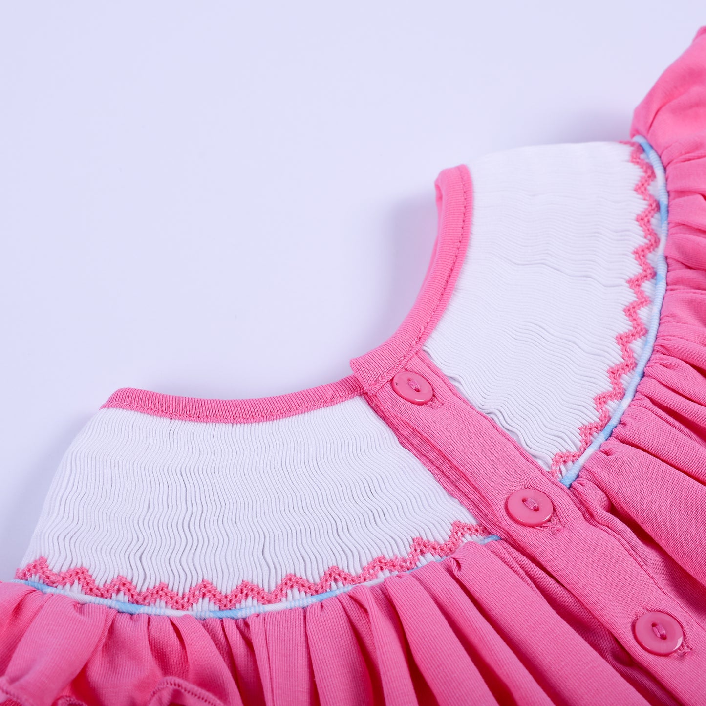 Close-up back button closure detail on pink hand-smocked knit baby girl top with ruffled neckline collar.