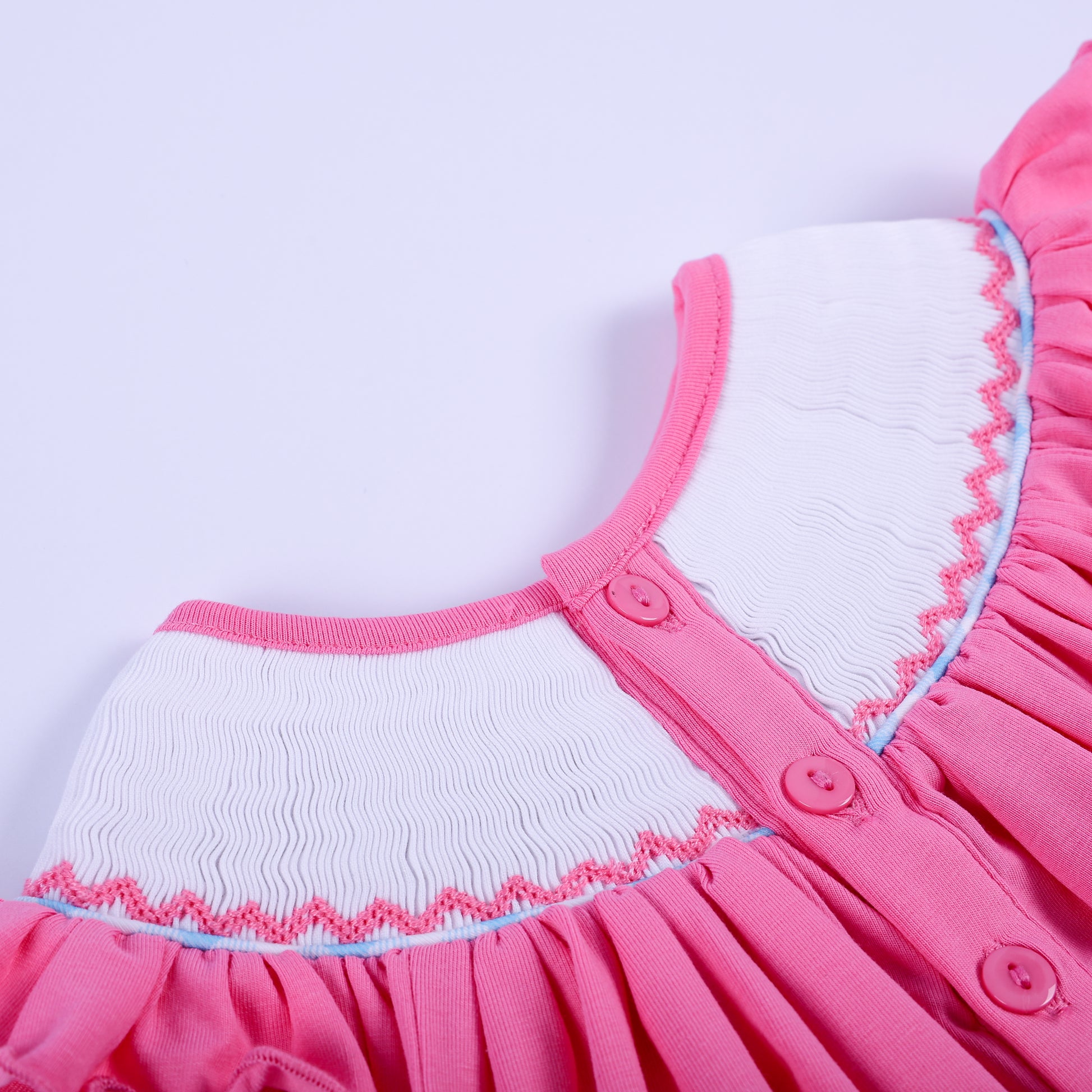 Close-up back button closure detail on pink hand-smocked knit baby girl top with ruffled neckline collar.