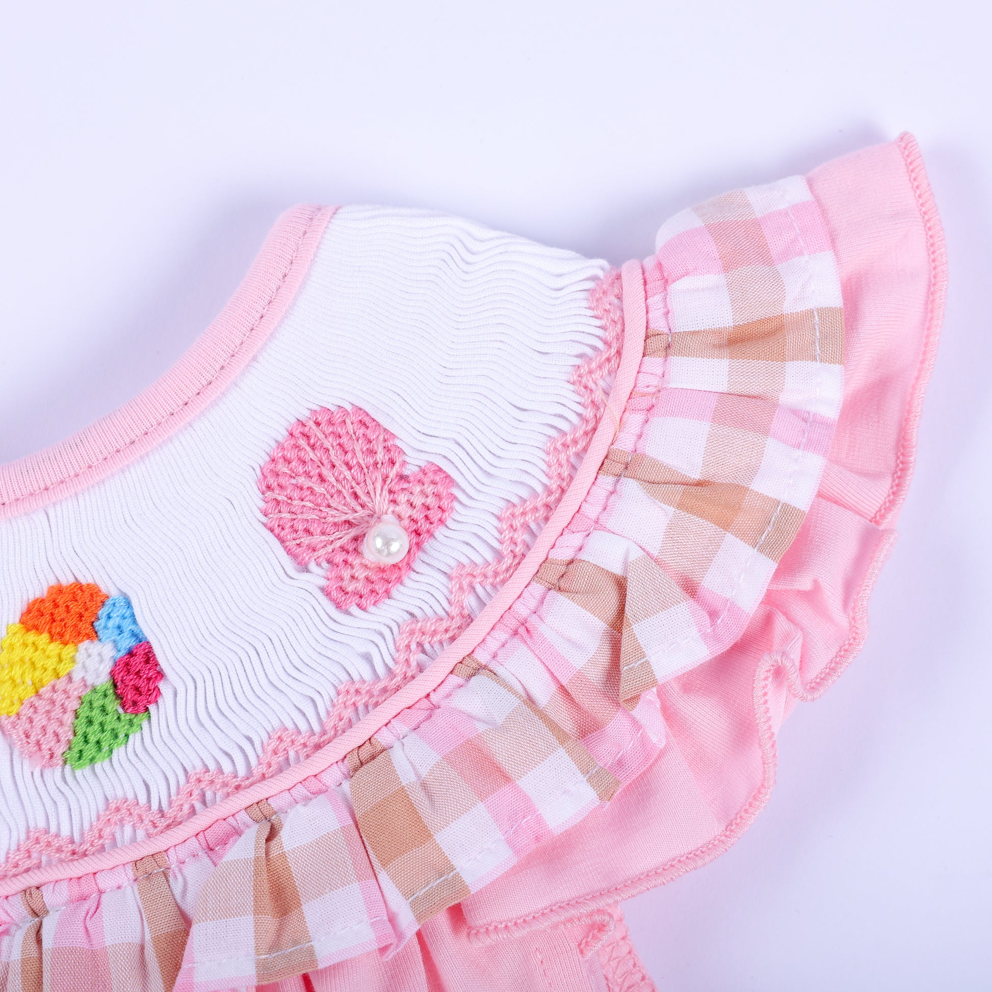 Close-up of hand embroidered pink seashell with pearl accent and gingham ruffle sleeve on baby smocked top.