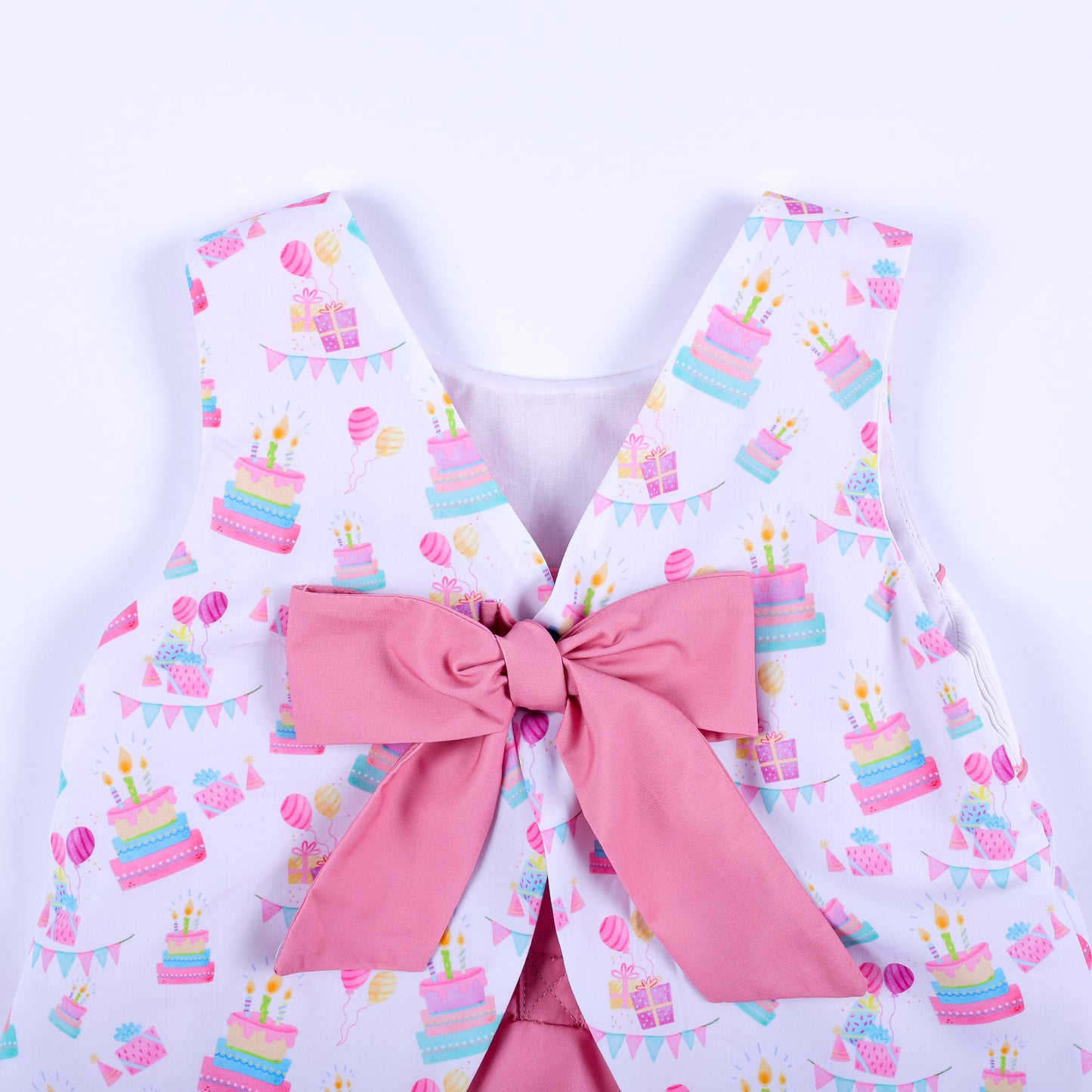 Close-up detail of the pink fabric tie bow on the back of a hand smocked birthday girl bubble romper.