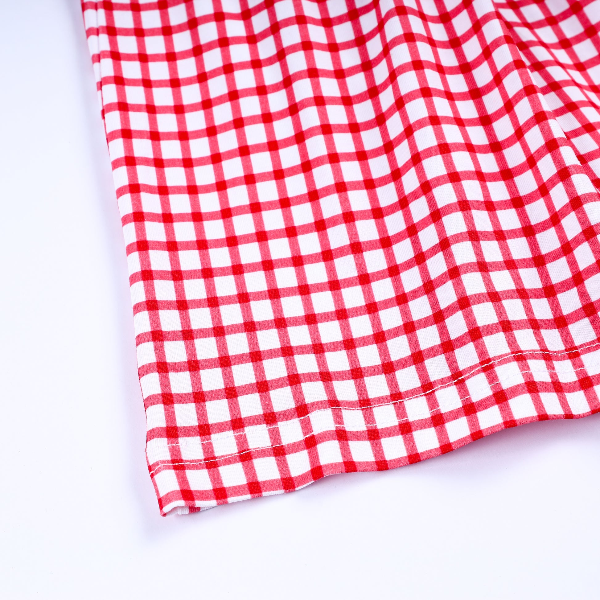 Close up view of red and white gingham pattern fabric and stitched hem detail on girls hand smocked dress.