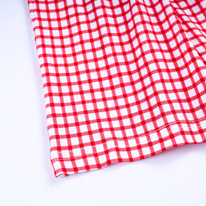 Close up view of red and white gingham pattern fabric and stitched hem detail on girls hand smocked dress.