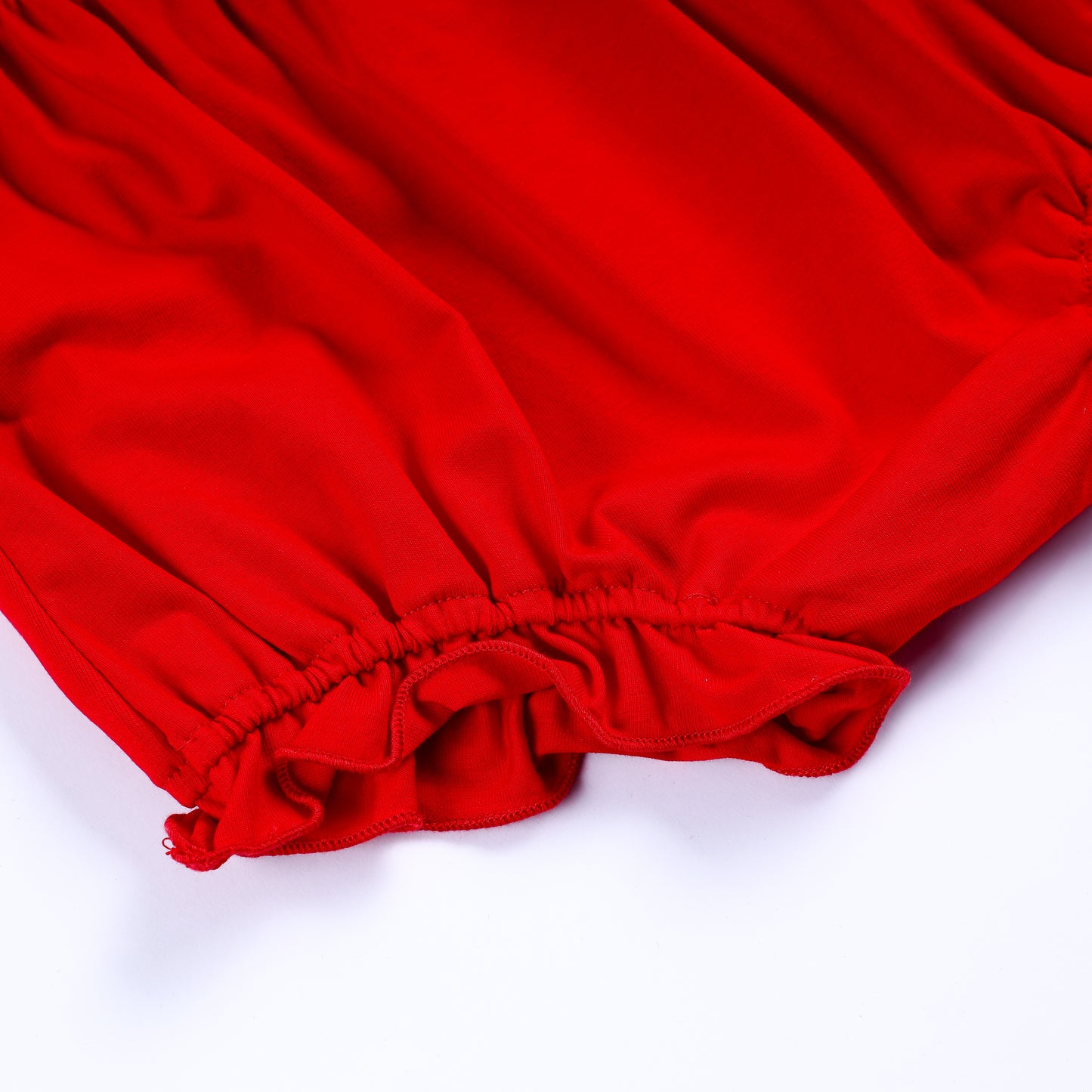 Detailed view of elastic ruffled leg ruffle on solid red diaper cover bloomer matching hand smocked outfit set.