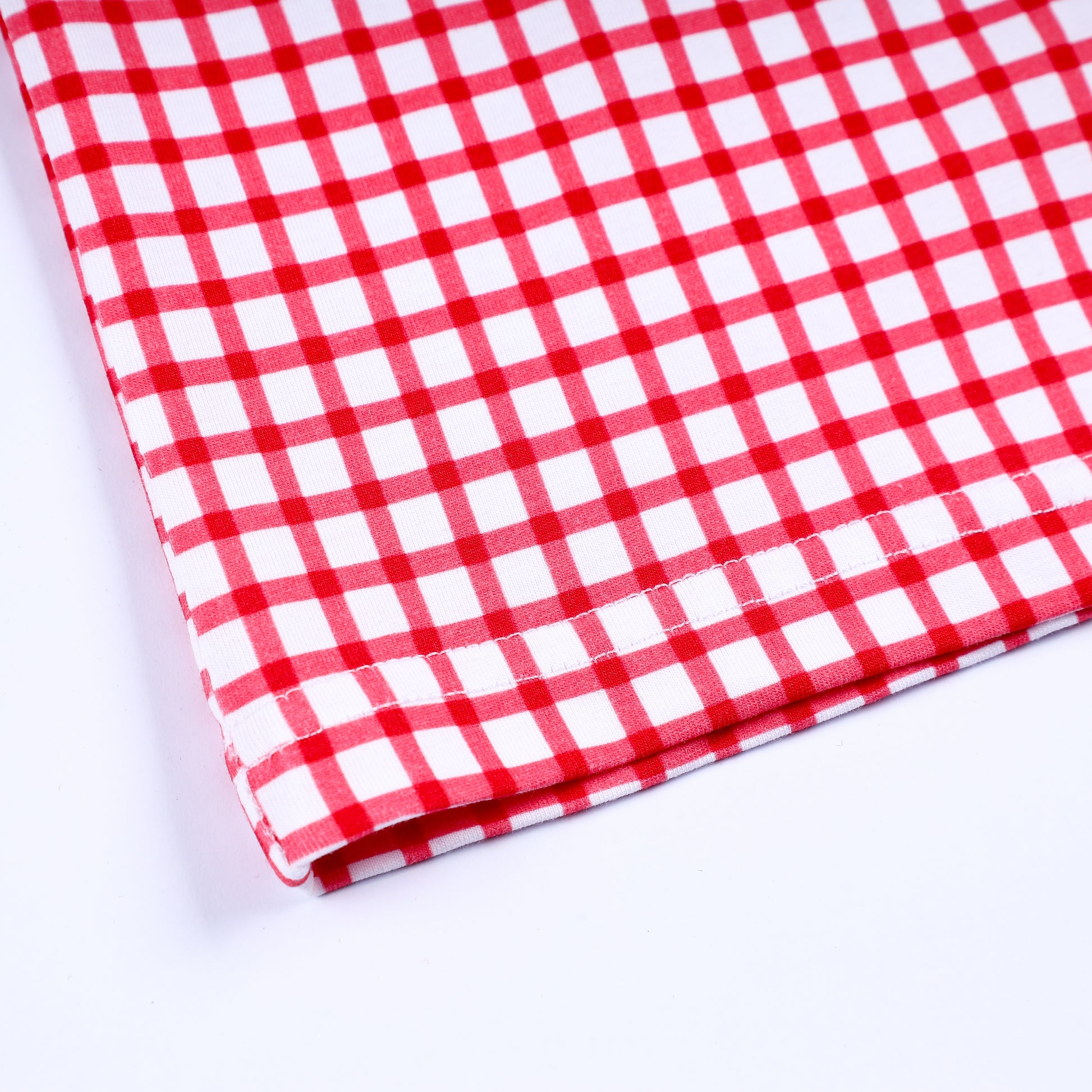 Close up view of bottom hem stitching and red gingham check cotton fabric on hand smocked boys short sleeve tee.