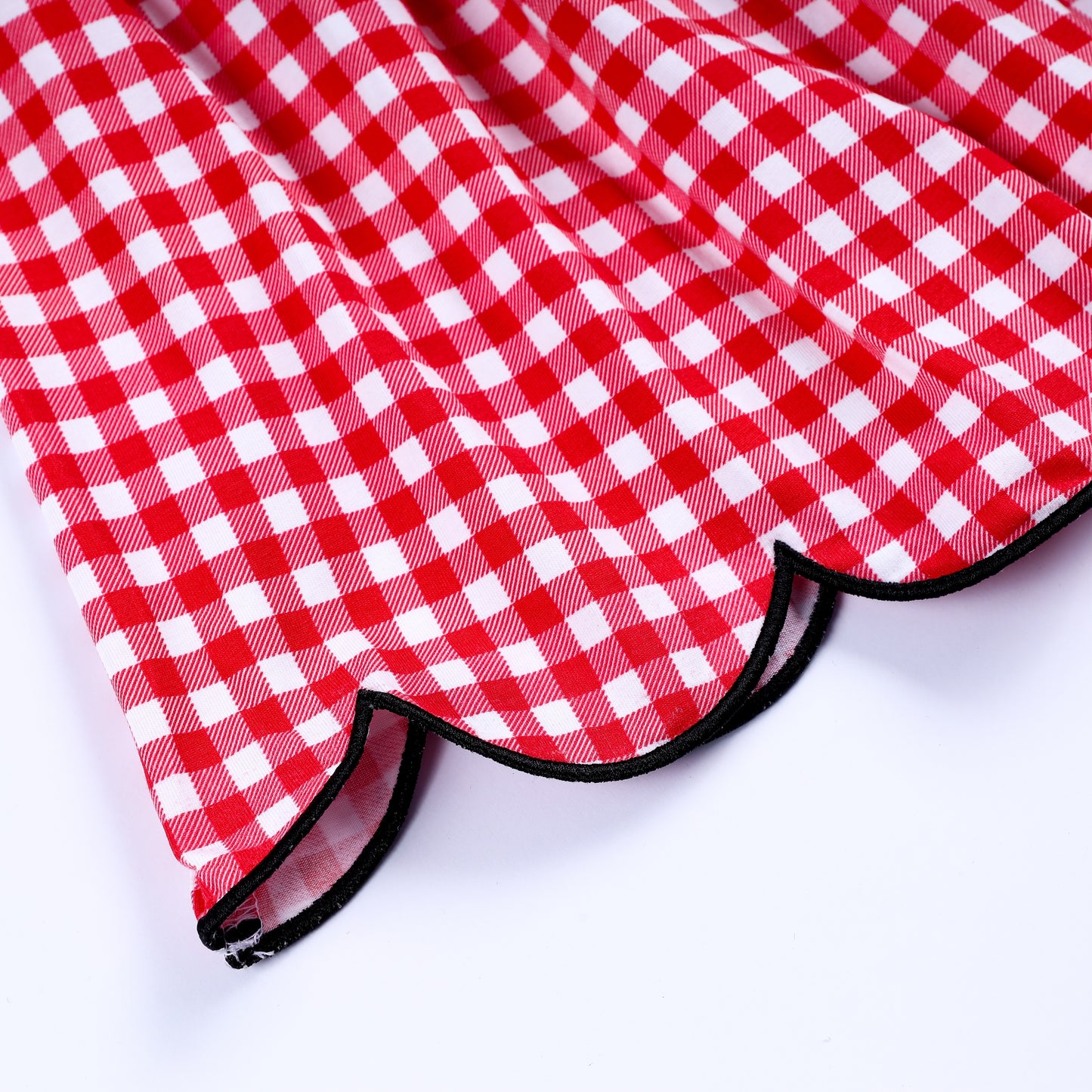 Detail of the black trimmed scalloped hemline on a classic red gingham hand smocked dress for children.