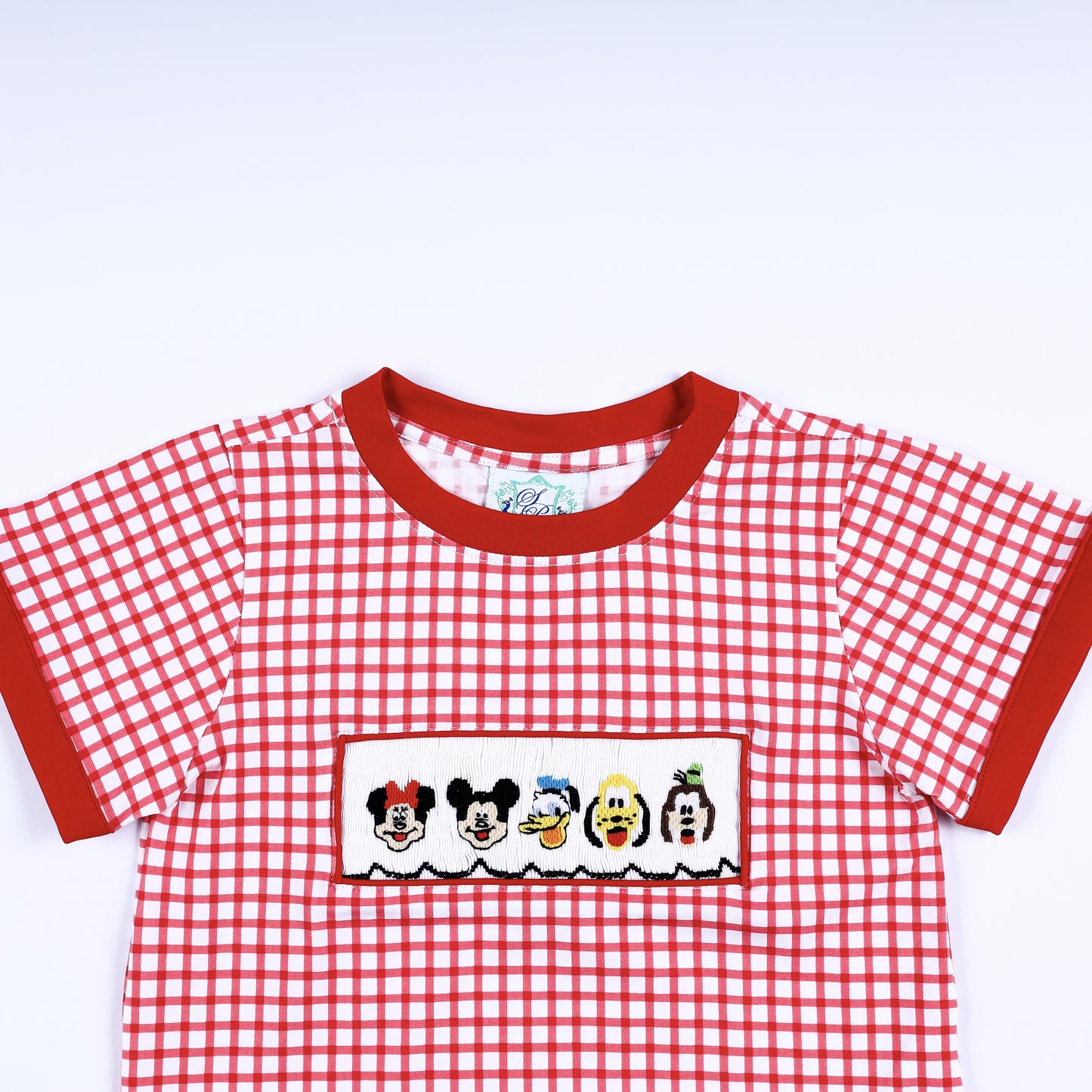 Close up view of the red crew neck collar and hand smocked cartoon character panel on a red gingham boys shirt.