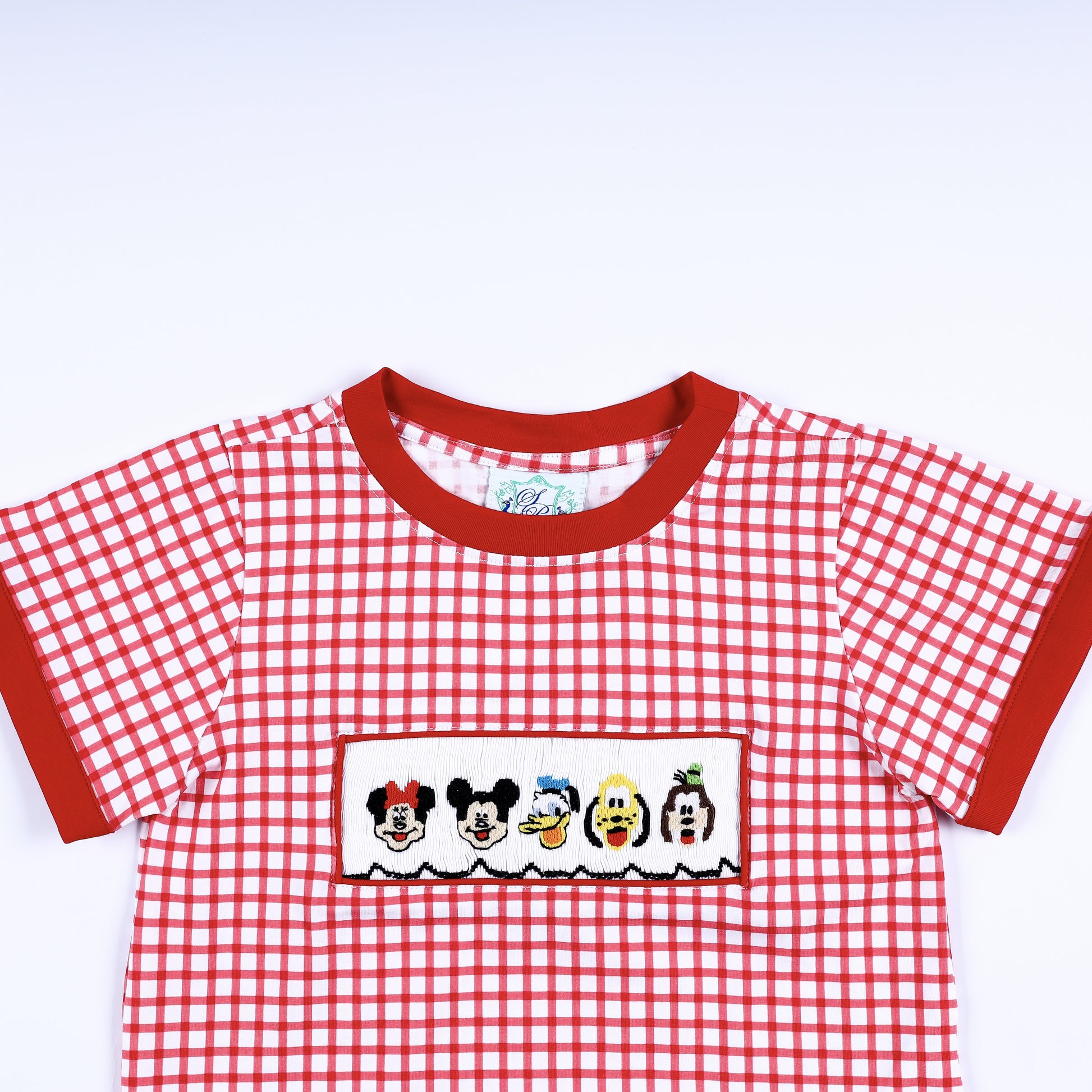 Close up view of the red crew neck collar and hand smocked cartoon character panel on a red gingham boys shirt.