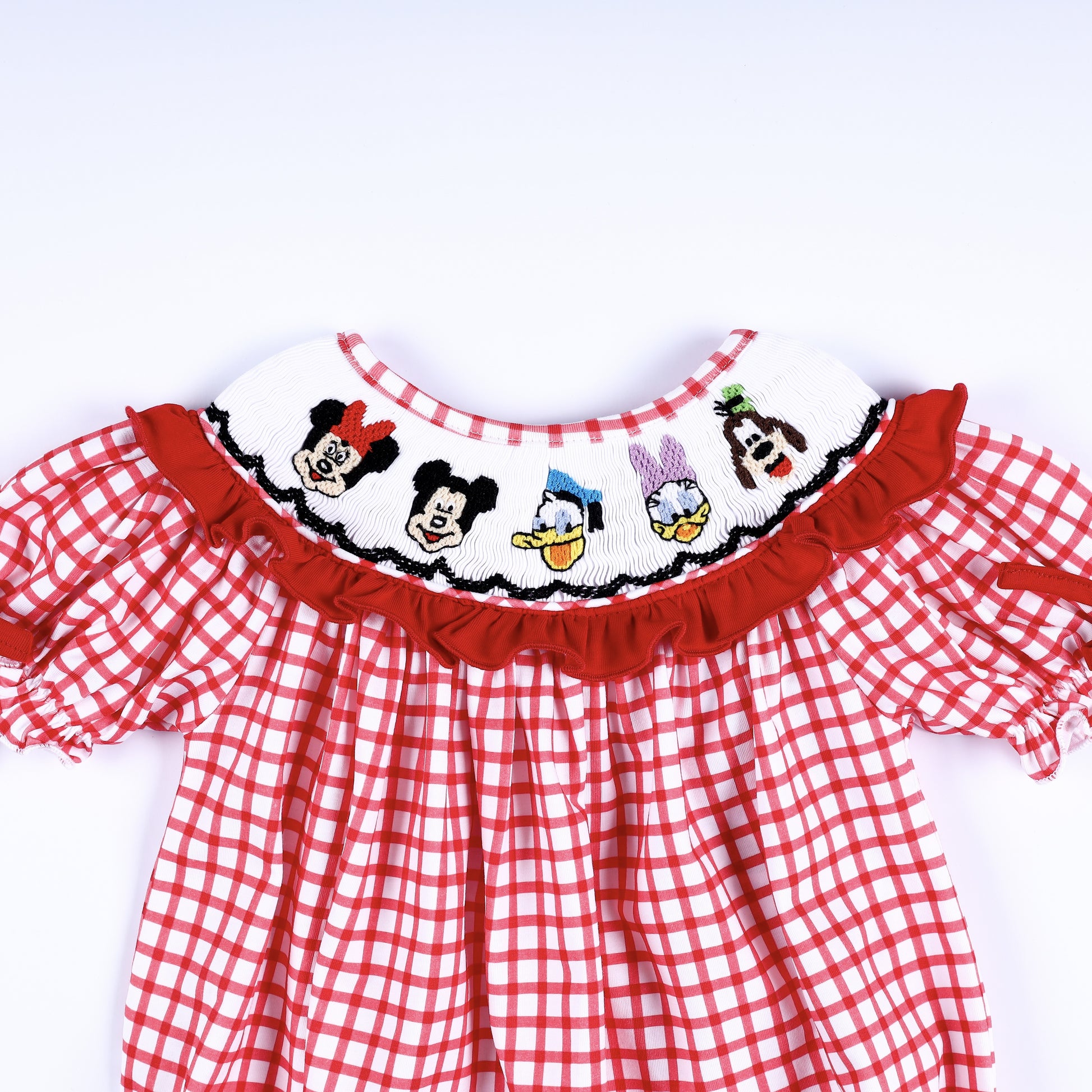 Front view of hand-smocked white collar with hand-embroidered character faces and red ruffle trim on baby bubble.