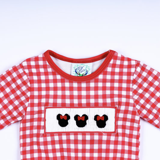 Close-up top view of red gingham long sleeve rash guard shirt with hand smocked Minnie Mouse bow embroidery plate.