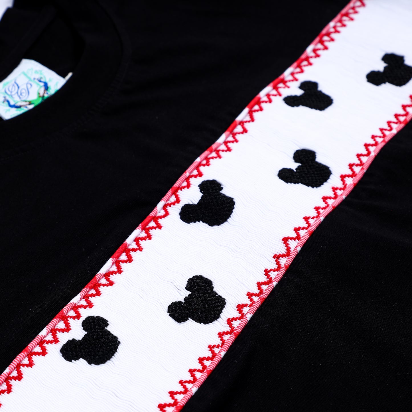 Detailed shot of hand embroidered black mouse heads on white smocked bodice with red smocking border.