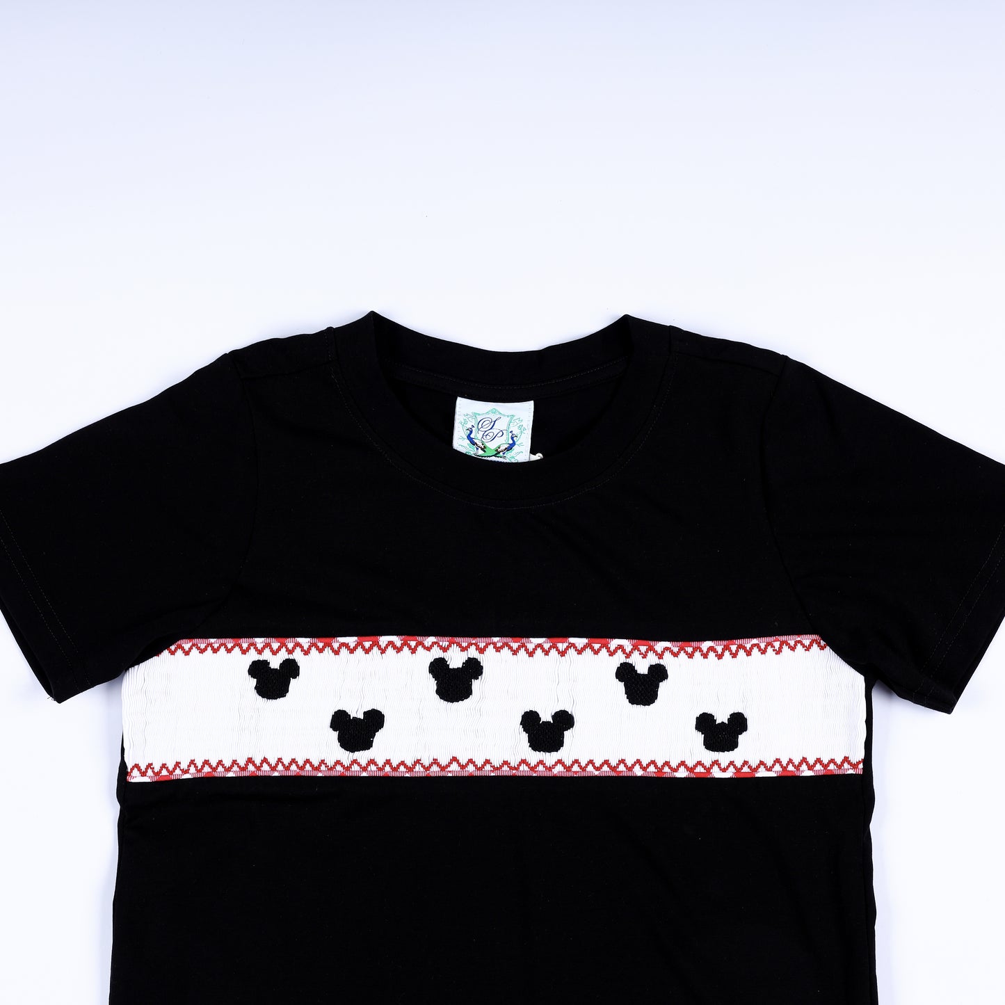 Close-up of hand smocked mouse silhouettes embroidered on white chest plate panel of black boys shirt.