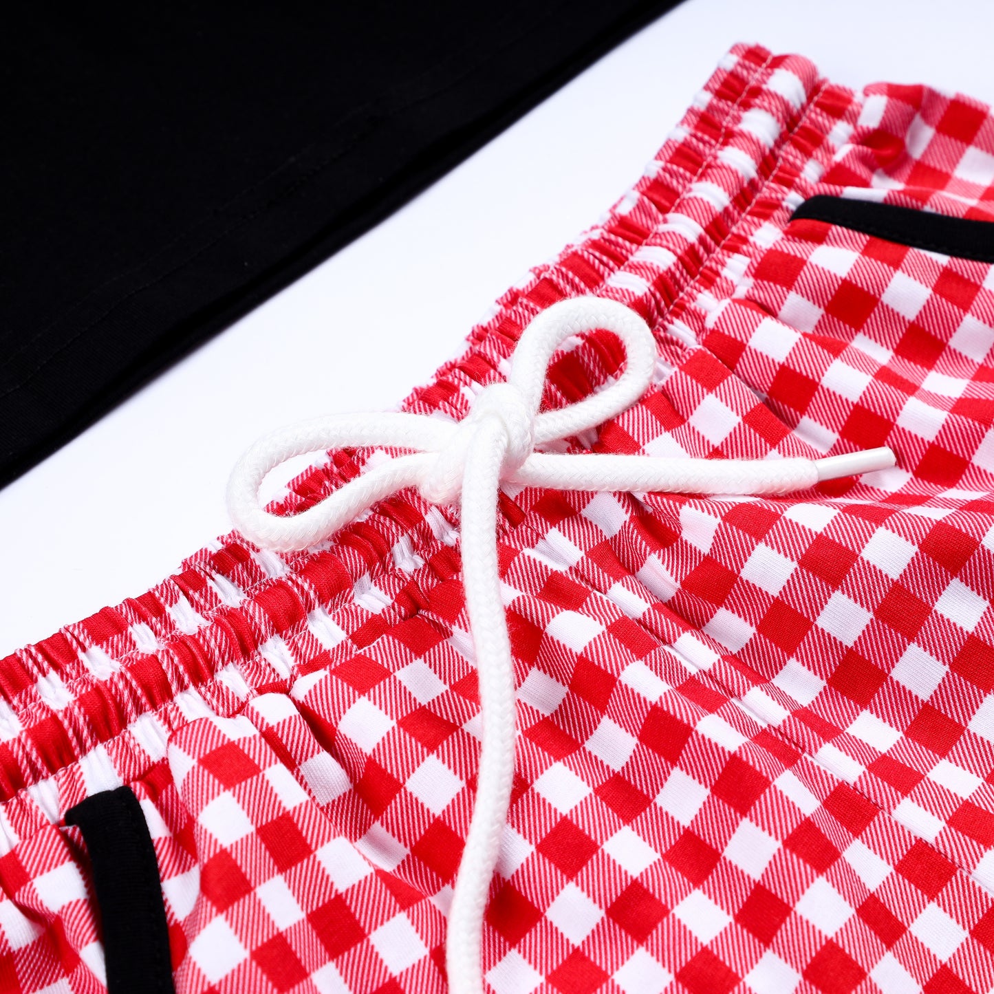 Close-up of white drawstring tie on the elastic waistband of red and white gingham smocked boys shorts.