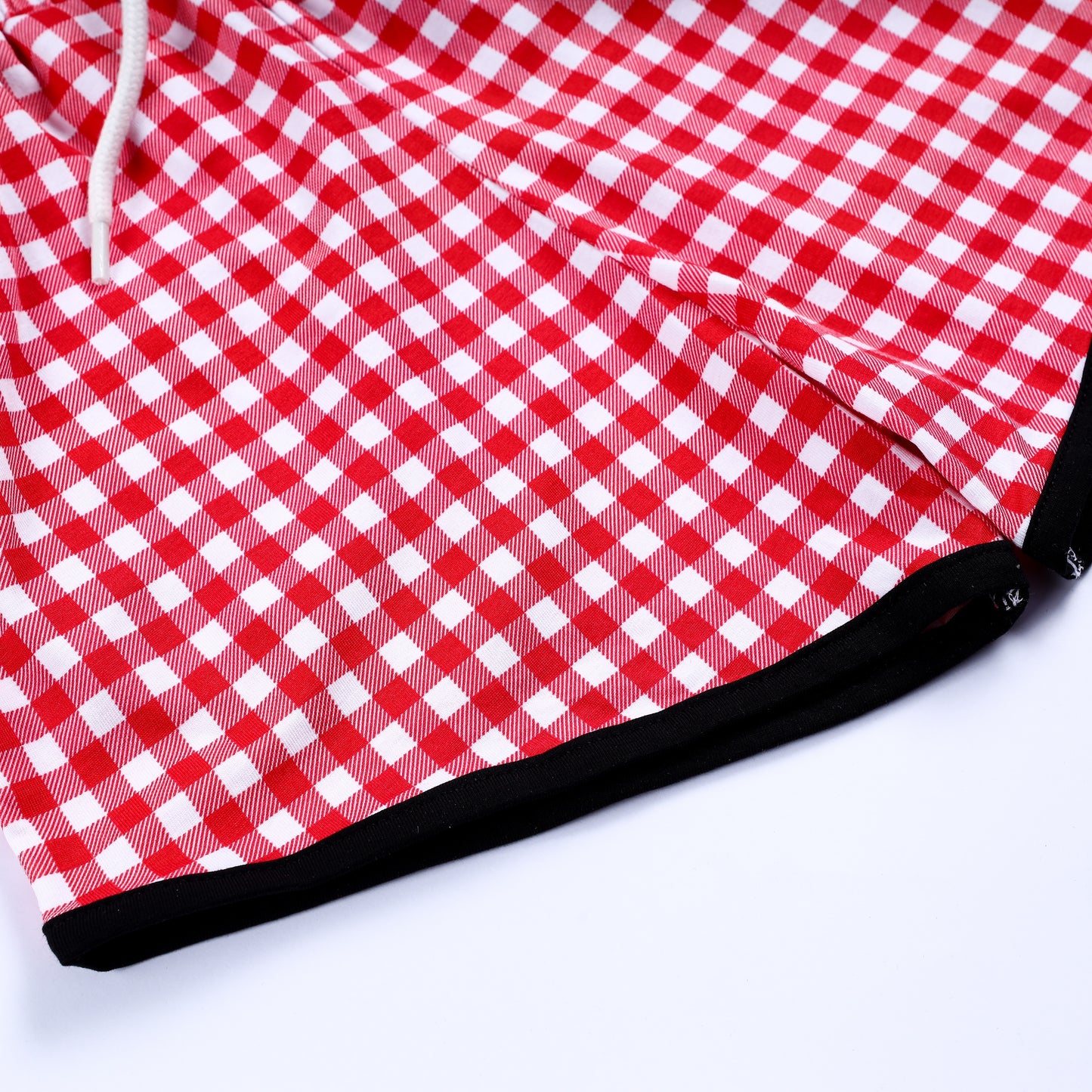 Close-up detail of red gingham check pattern fabric and black hem trim on smocked boys outfit shorts.