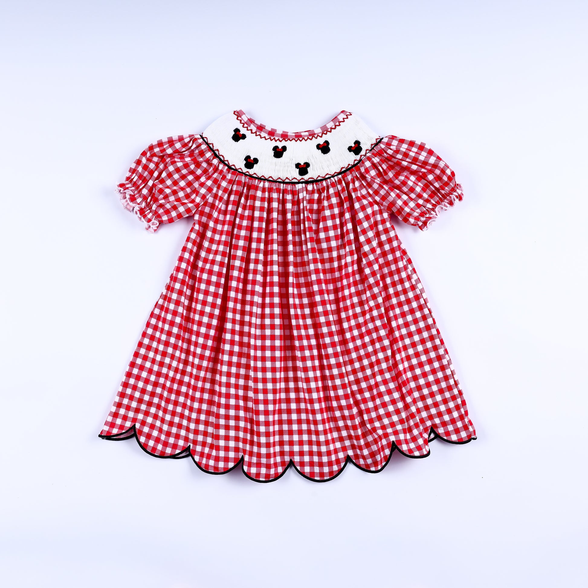 Red gingham mouse hand smocked dress for girls featuring puff sleeves and a scalloped black trimmed hem.