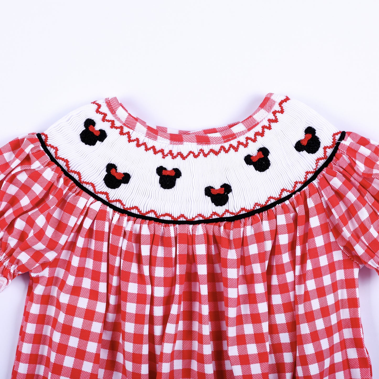 Close up of hand smocked white collar featuring hand embroidered black mouse heads with red bows on red gingham.