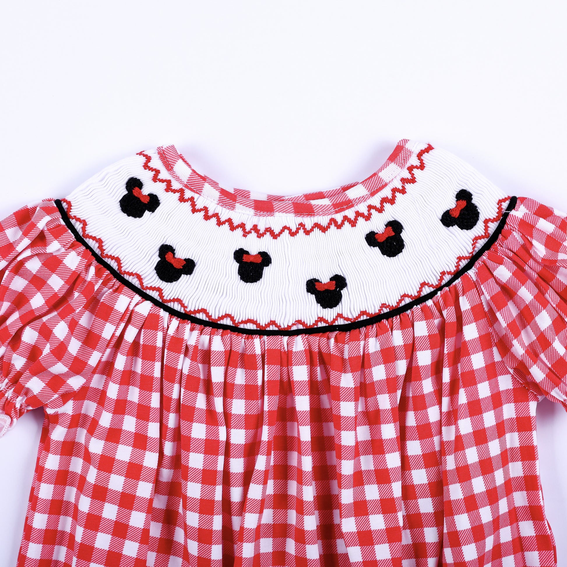 Close up of hand smocked white collar featuring hand embroidered black mouse heads with red bows on red gingham.