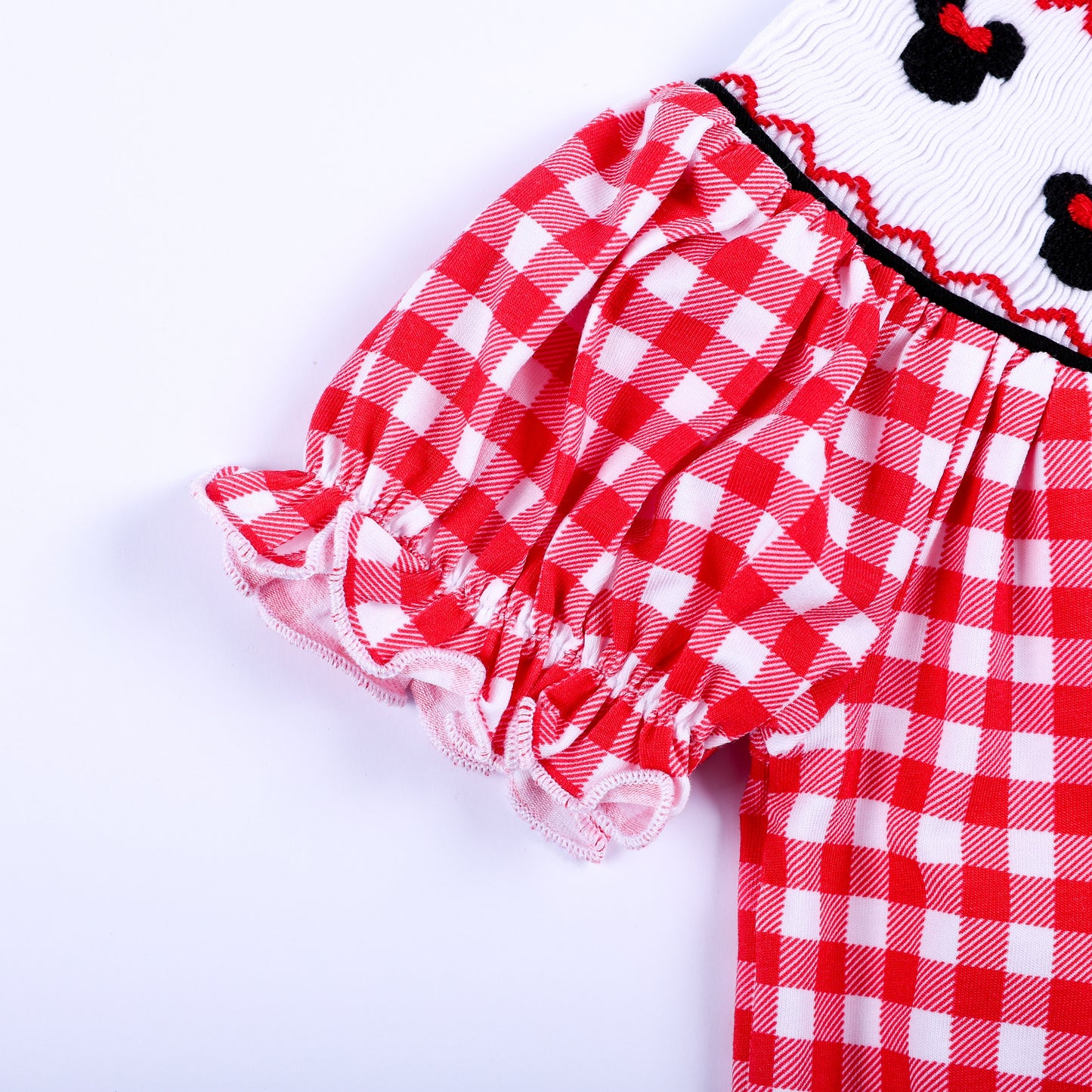 Detailed close up of ruffled puffed short sleeve on red and white gingham baby girl hand smocked bubble romper.
