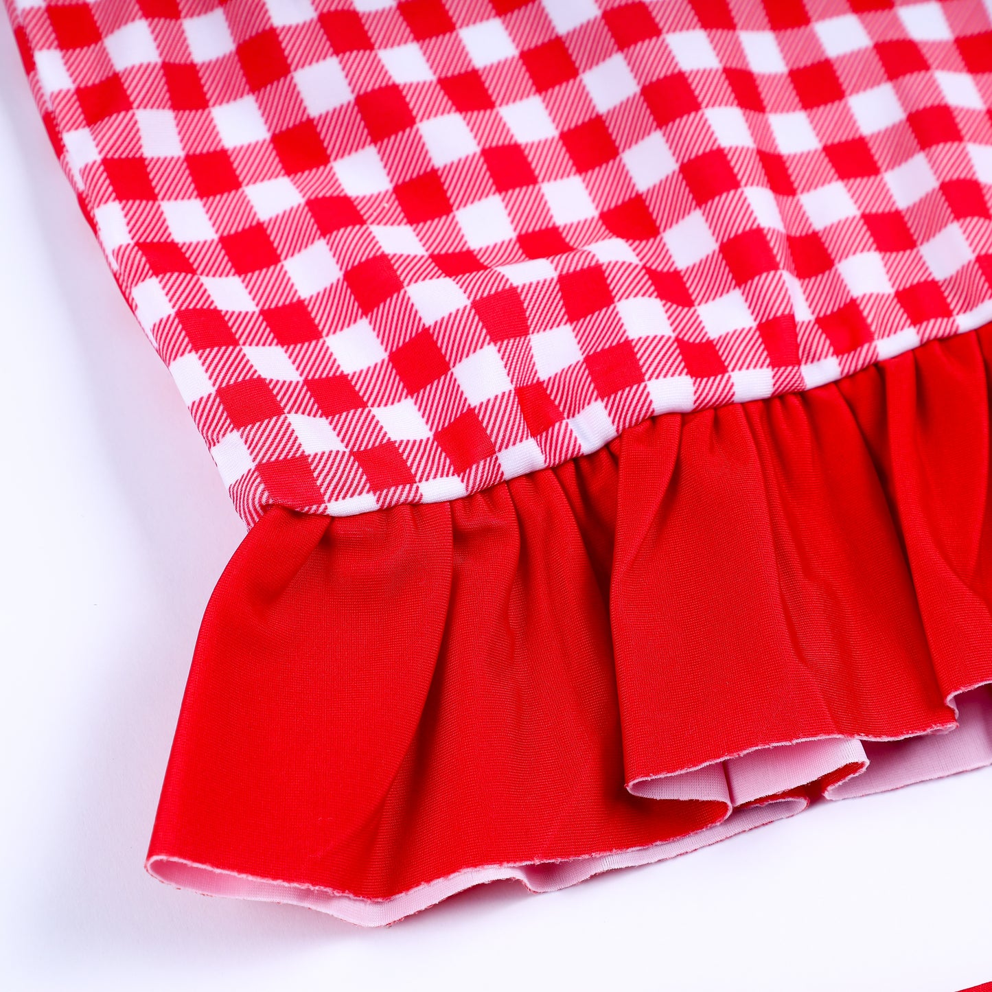 Close-up view of solid red ruffle trim hem on girls red gingham long sleeve smocked rash guard swimsuit top.