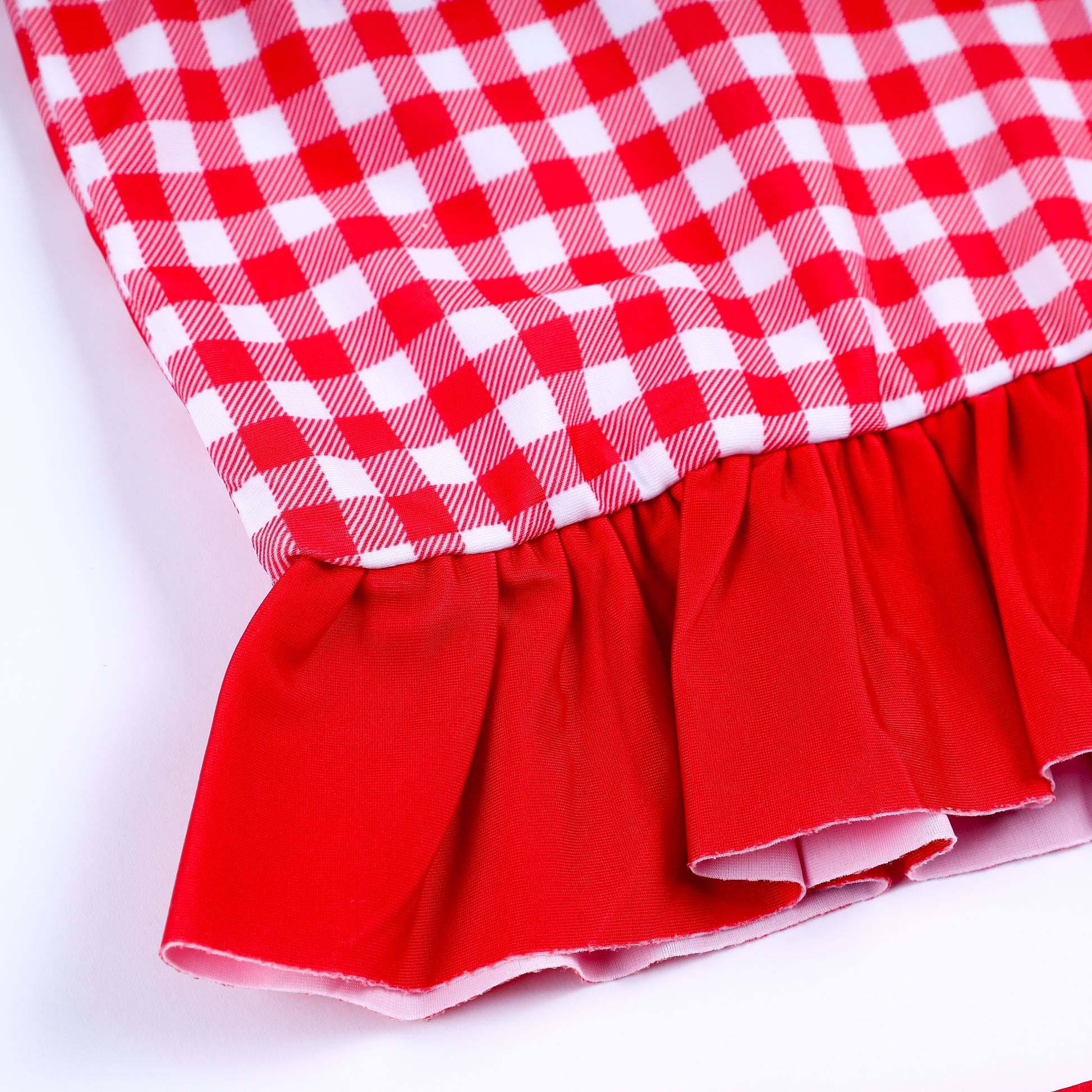 Close-up view of solid red ruffle trim hem on girls red gingham long sleeve smocked rash guard swimsuit top.