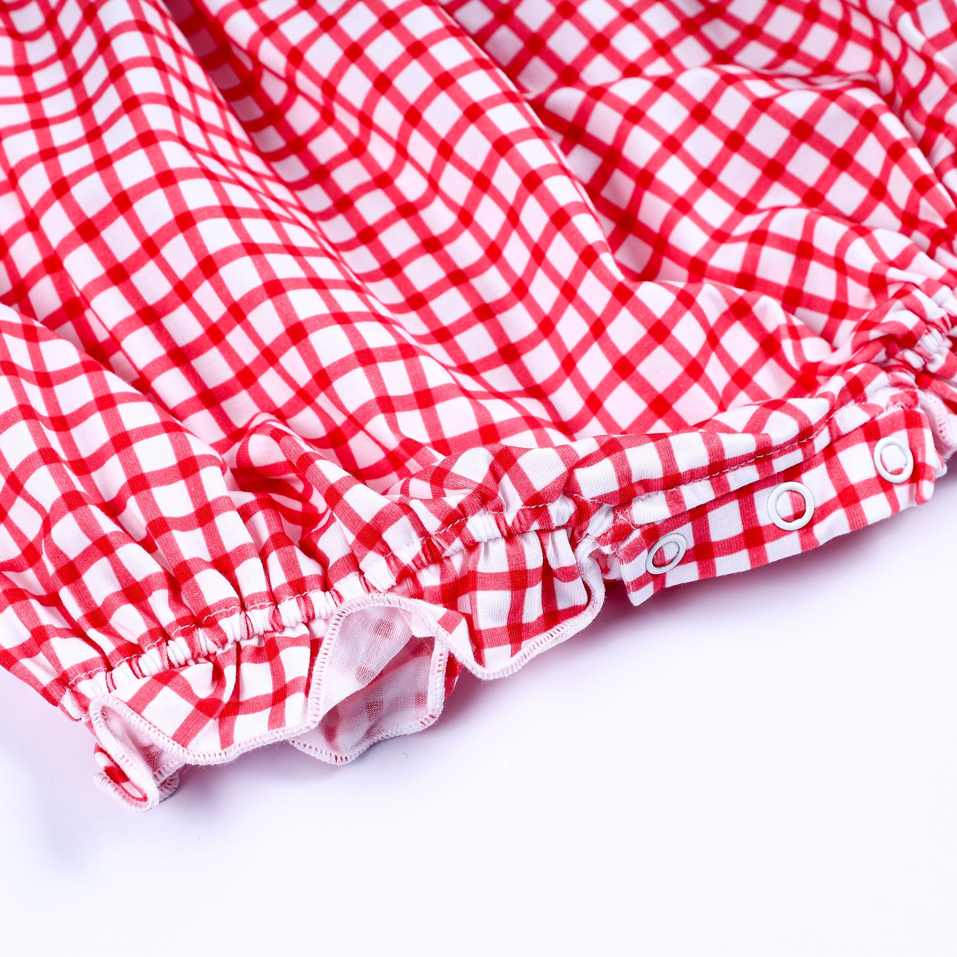 Close-up of bottom snap buttons and ruffled elastic leg openings on a red gingham hand-smocked baby bubble romper.