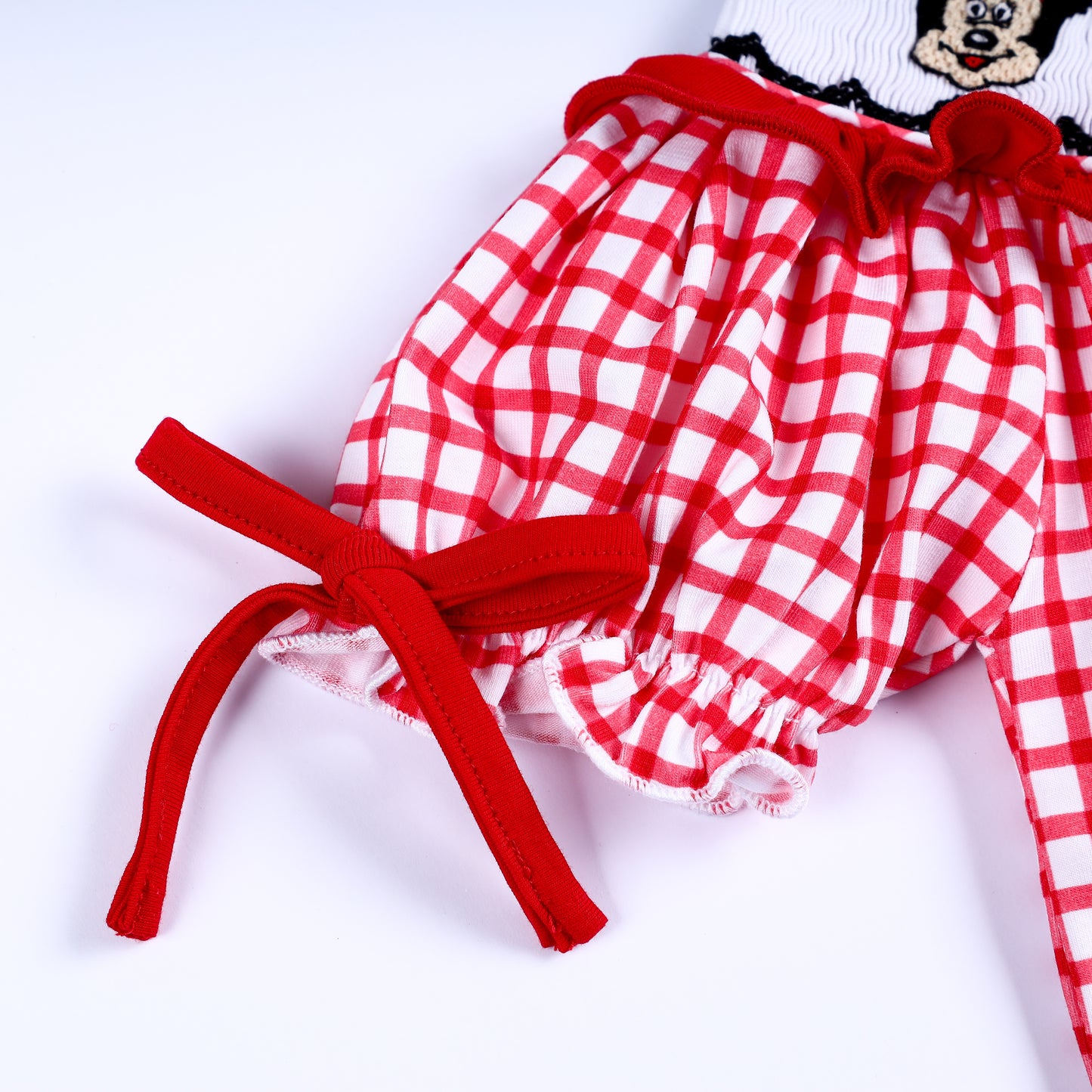 Close-up detail of ruffled puff sleeve with a red fabric tie bow on a red gingham hand-smocked baby bubble outfit.