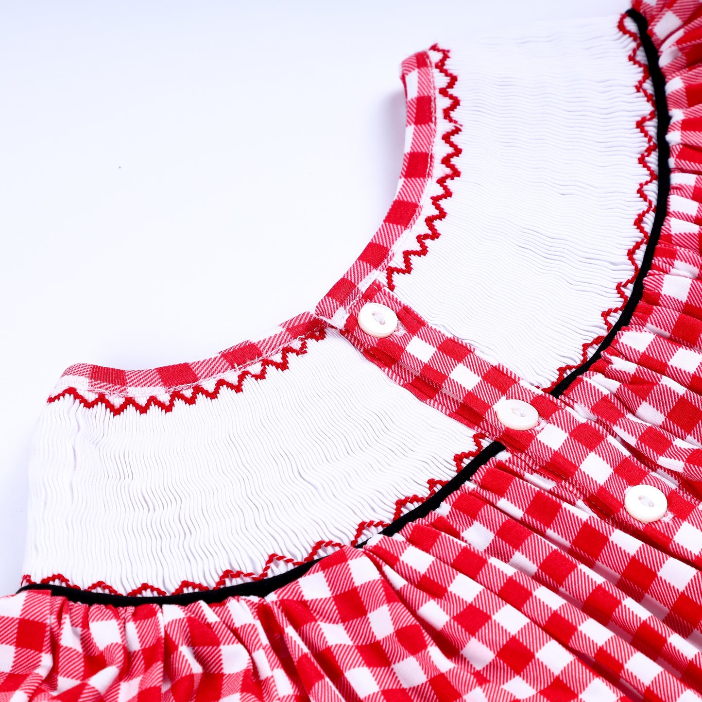 Close-up of the white button back closure and delicate red zig-zag stitching on a hand-smocked collar.