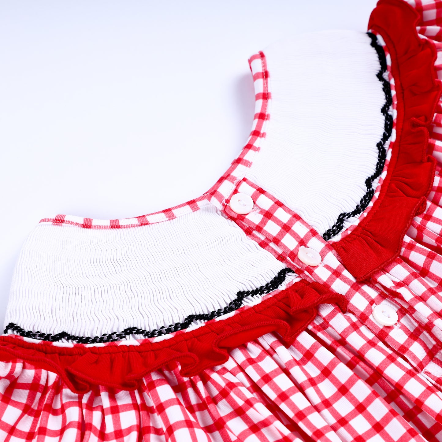 Close-up of back button closure placket and white smocked collar trim on red gingham hand smocked baby dress.