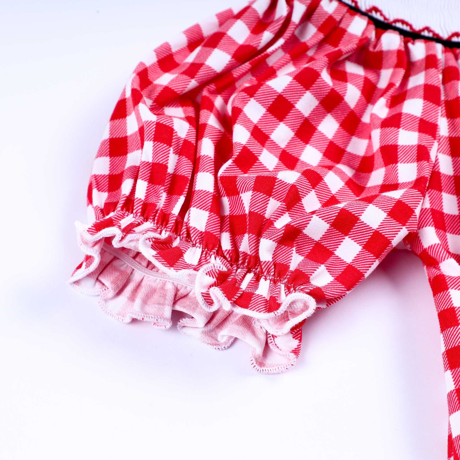 Detailed view of the ruffled puff sleeve on a red gingham hand-smocked dress for toddler and young girls.