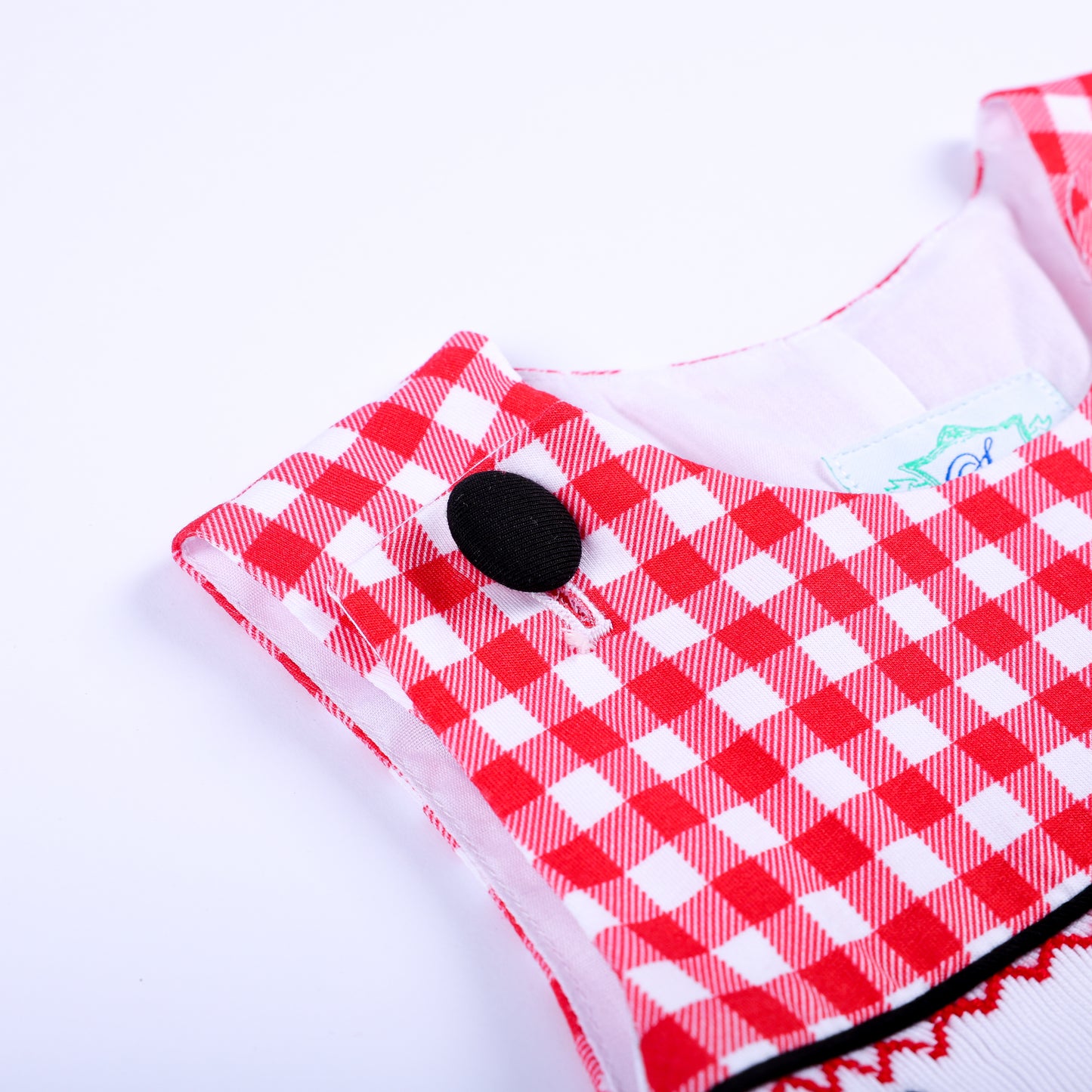 Close-up detail of black shoulder button closure and stitching on red gingham smocked boys jon jon cotton outfit.