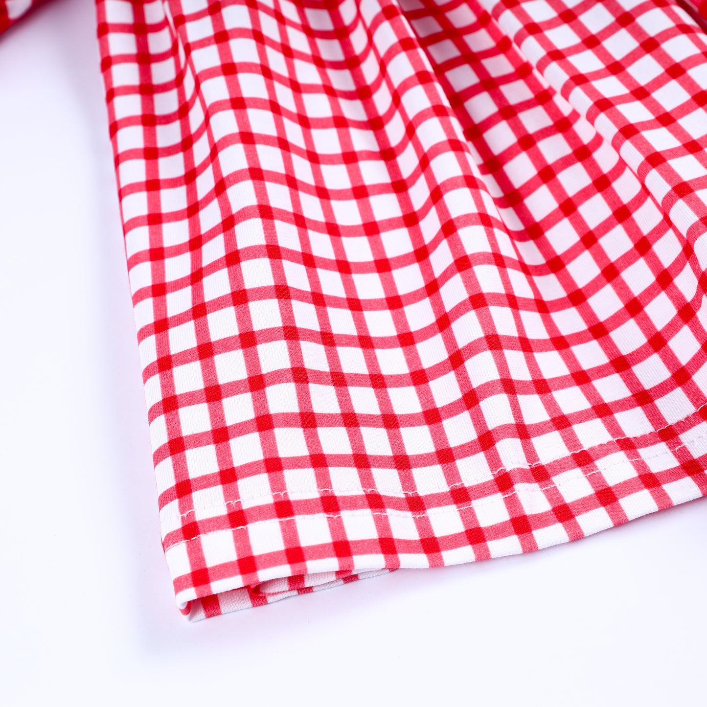 Close-up view of hemline stitching and premium red and white gingham pattern fabric of smocked toddler dress.