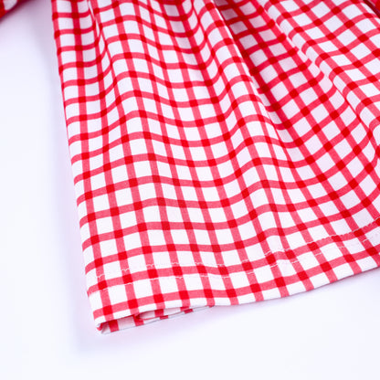 Close-up view of hemline stitching and premium red and white gingham pattern fabric of smocked toddler dress.