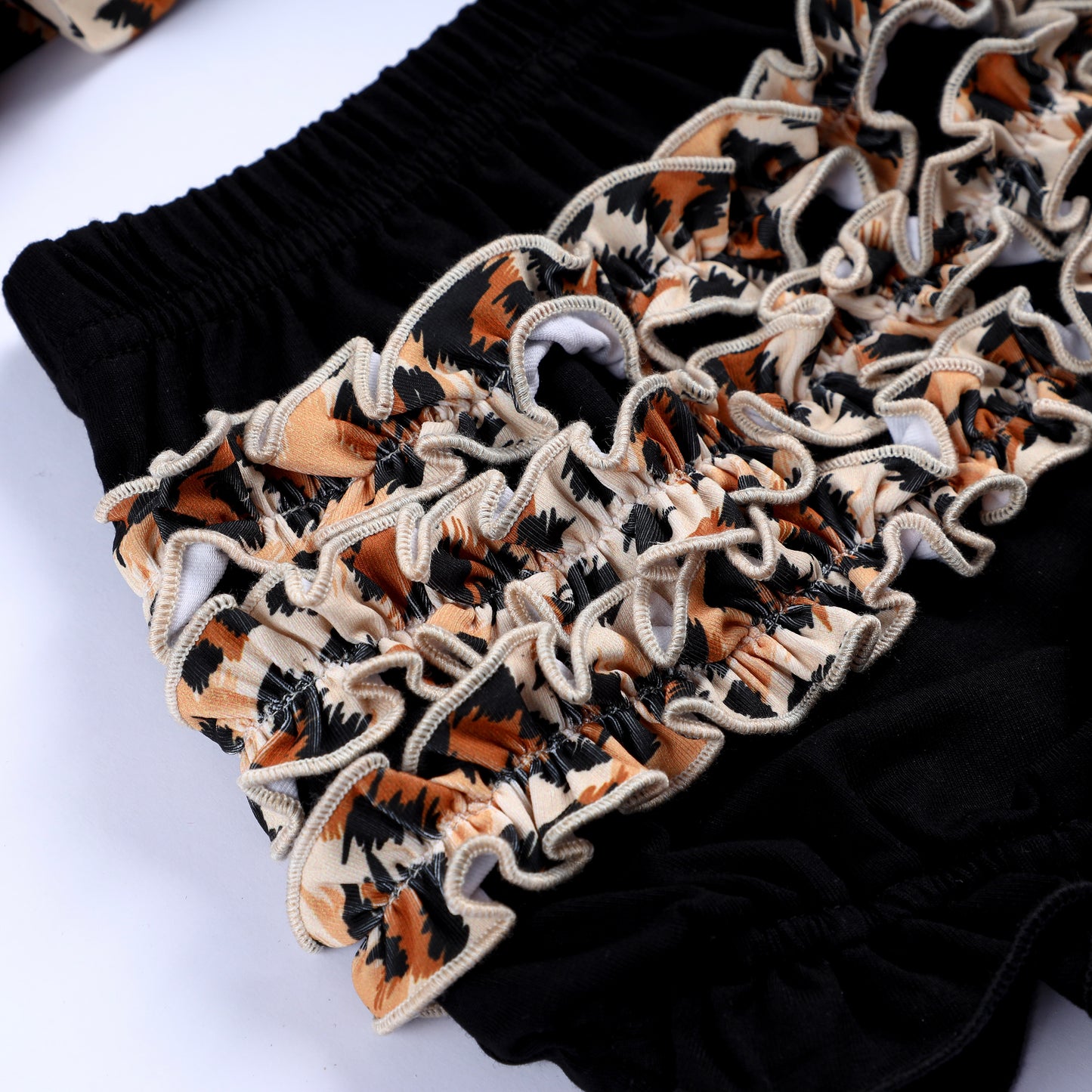 Detailed view of layered leopard animal print ruffles on black hand smocked bloomer set for baby and toddler girls.