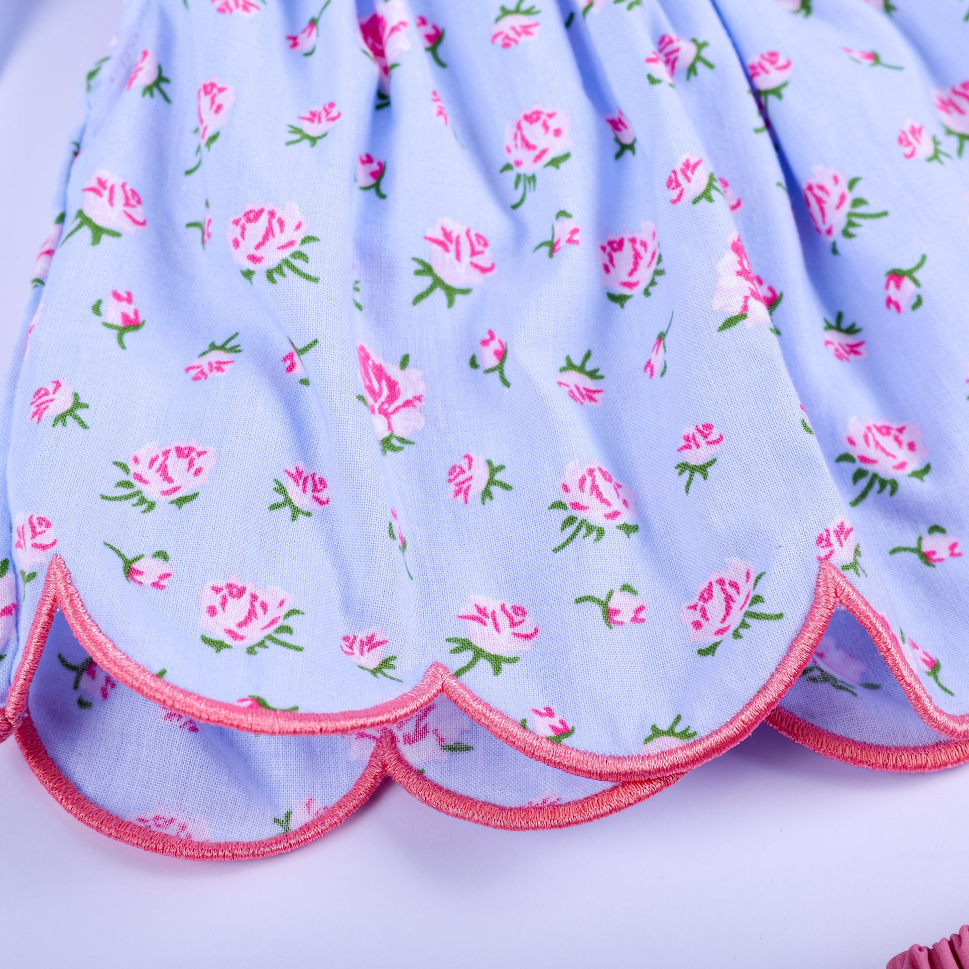 Detail shot of scalloped edge hemline with pink trim on blue floral hand smocked baby girl tunic top.