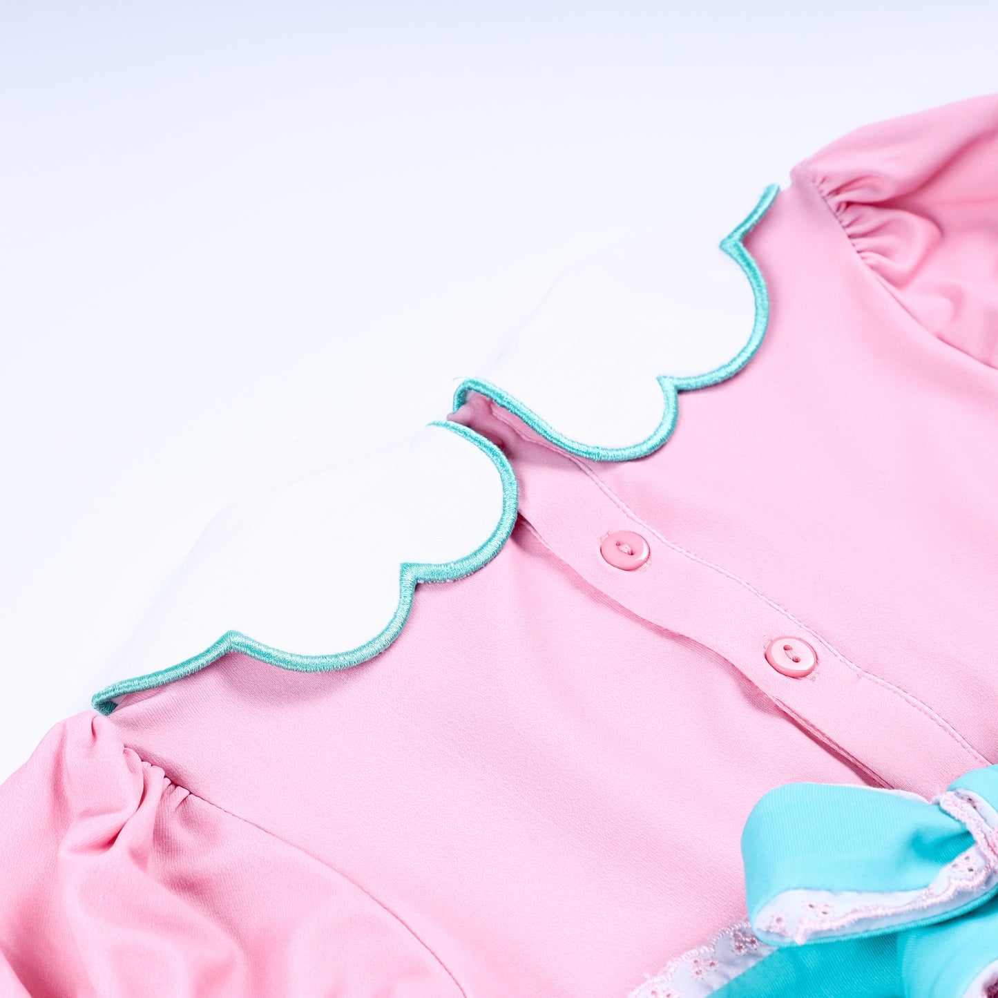 Close-up of scalloped Peter Pan collar with teal trim and back buttons on pink smocked baby girl bubble romper.