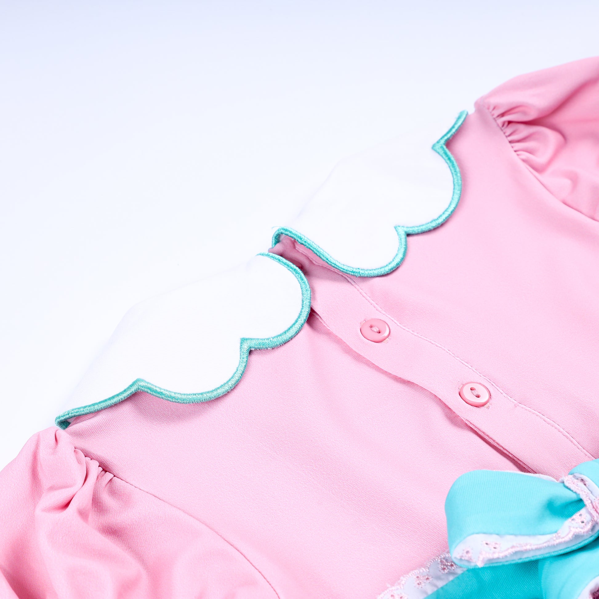 Close-up of scalloped Peter Pan collar with teal trim and back buttons on pink smocked baby girl bubble romper.