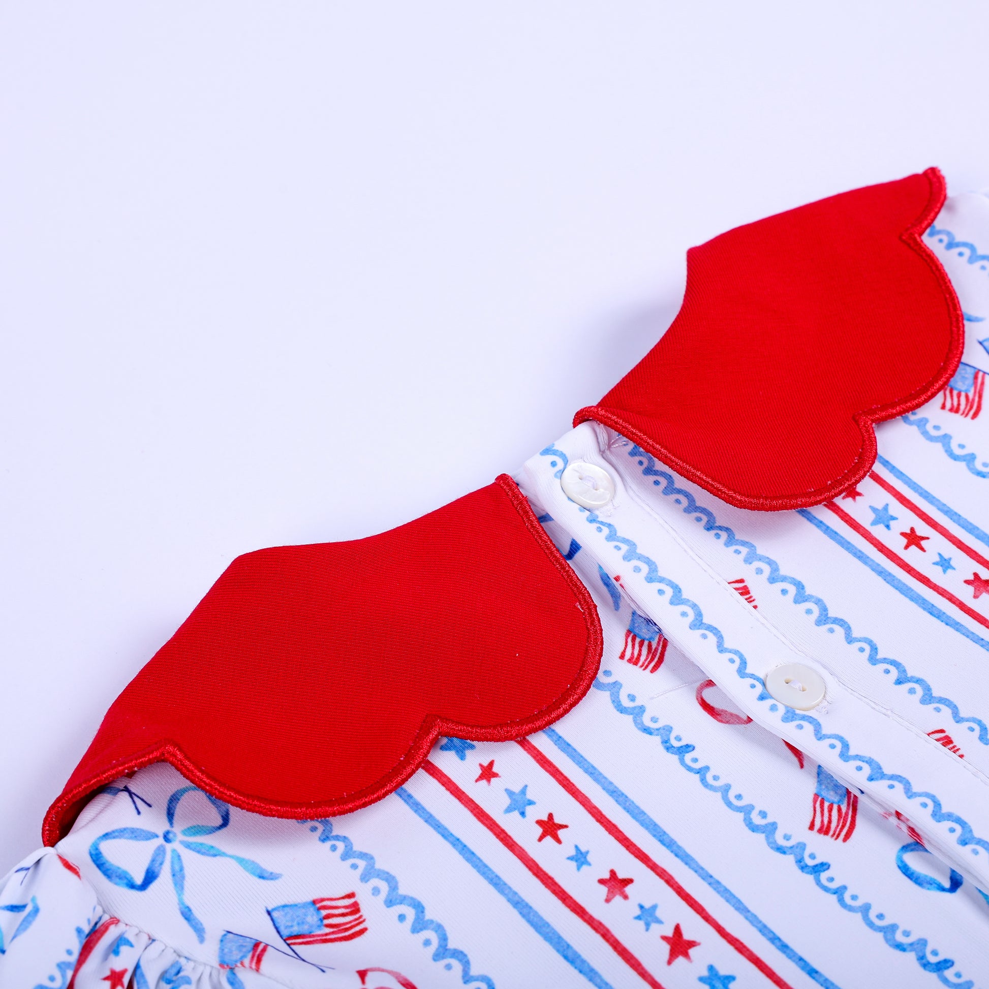 Close up shot of the back button placket and red scalloped collar details on patriotic smocked infant clothing set.