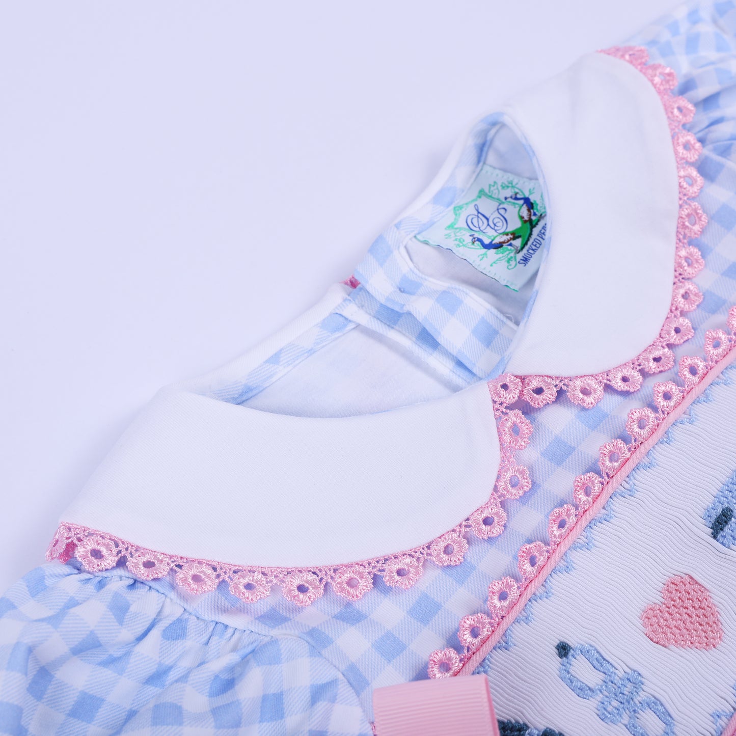 Angled close-up of the white Peter Pan collar with delicate pink lace trim on the blue gingham baby shower romper.