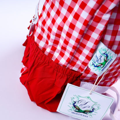 Side view of red gingham ruffle backpack showing side elastic pocket, white zipper, and brand hangtag.