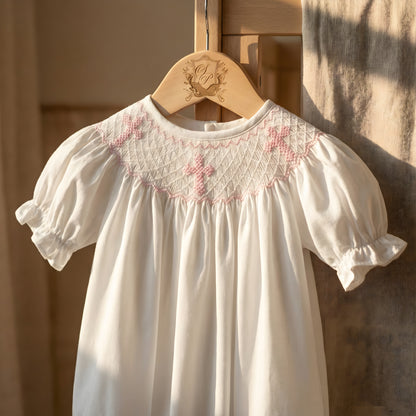 White girl bubble romper with hand-smocked pink embroidered crosses on the yoke. Traditional style for christening or baptism.