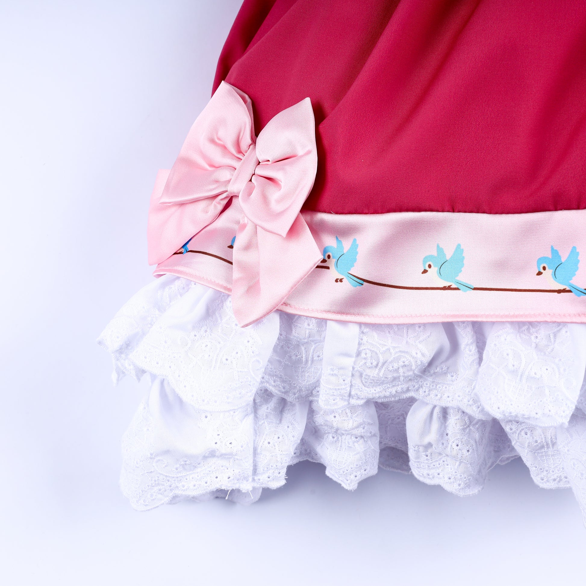 Close up of skirt hem featuring pink bow accent, blue bird ribbon trim, and eyelet lace ruffles on dress.