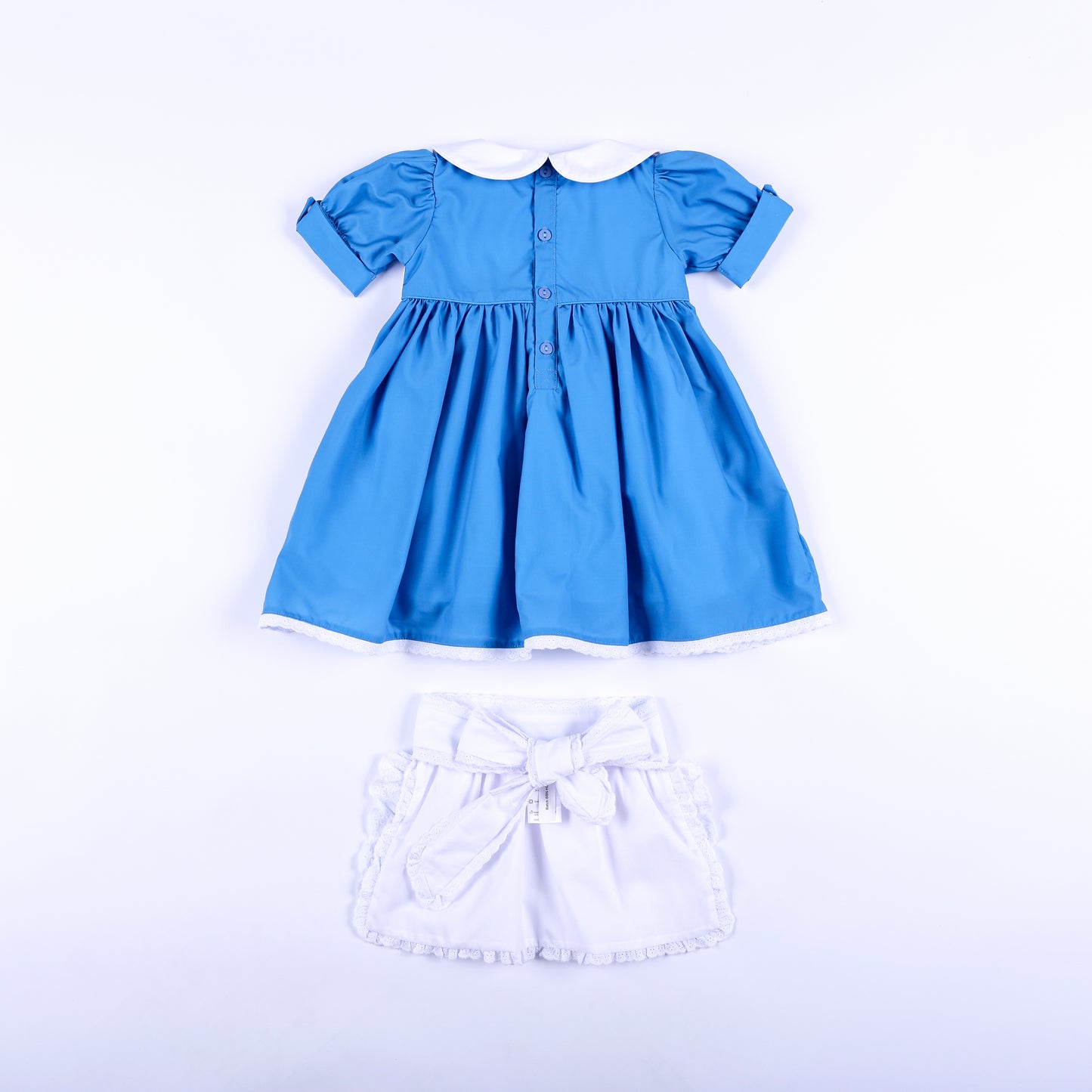 Back view of storybook wonderland blue dress with button back and white embroidered apron with bow tie.
