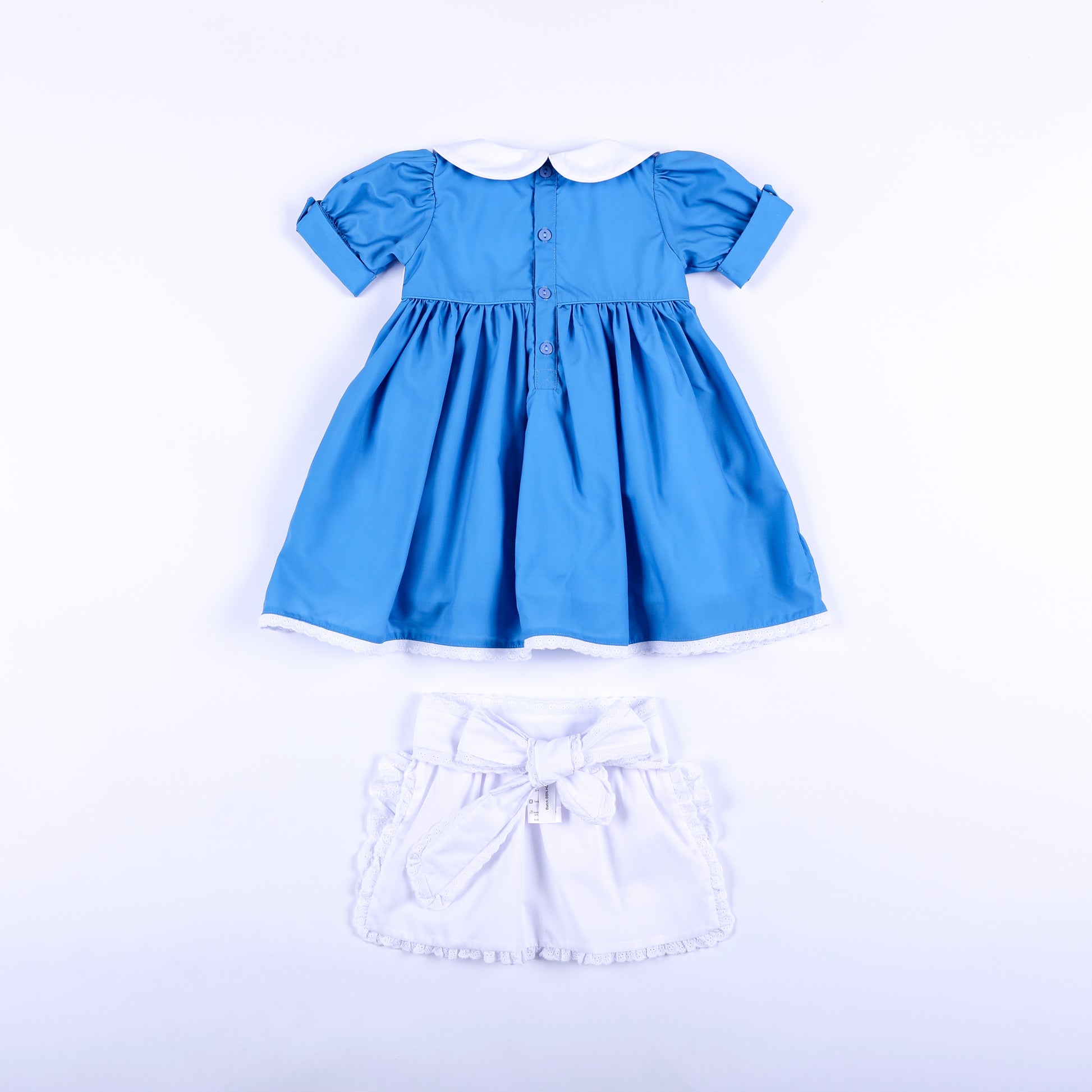 Back view of storybook wonderland blue dress with button back and white embroidered apron with bow tie.