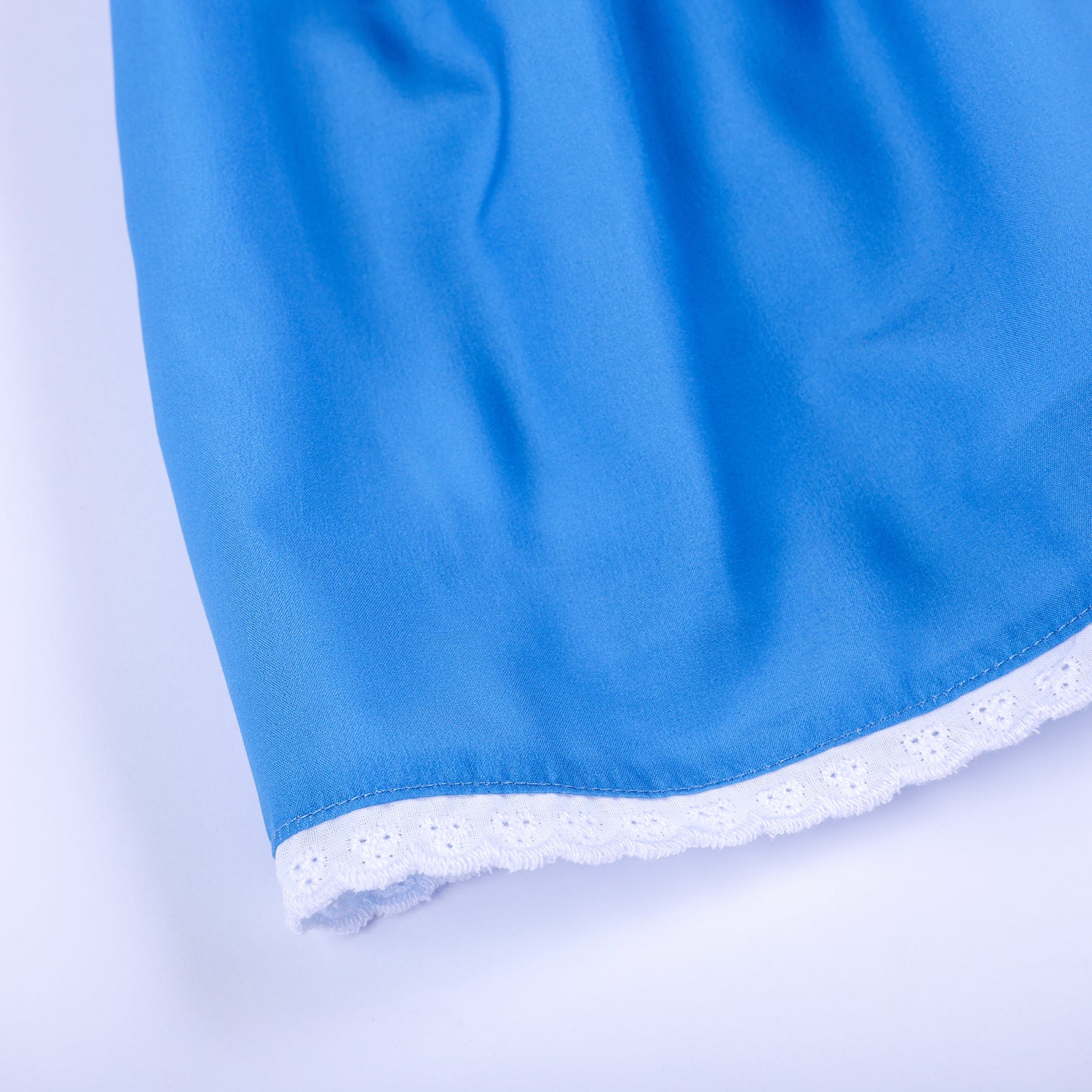 Close-up view of delicate white eyelet lace trimming along the bottom hem of blue smocked girls dress.