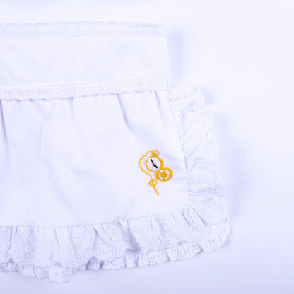 Detailed view of white eyelet lace ruffled apron featuring hand embroidered golden pocket watch motif.