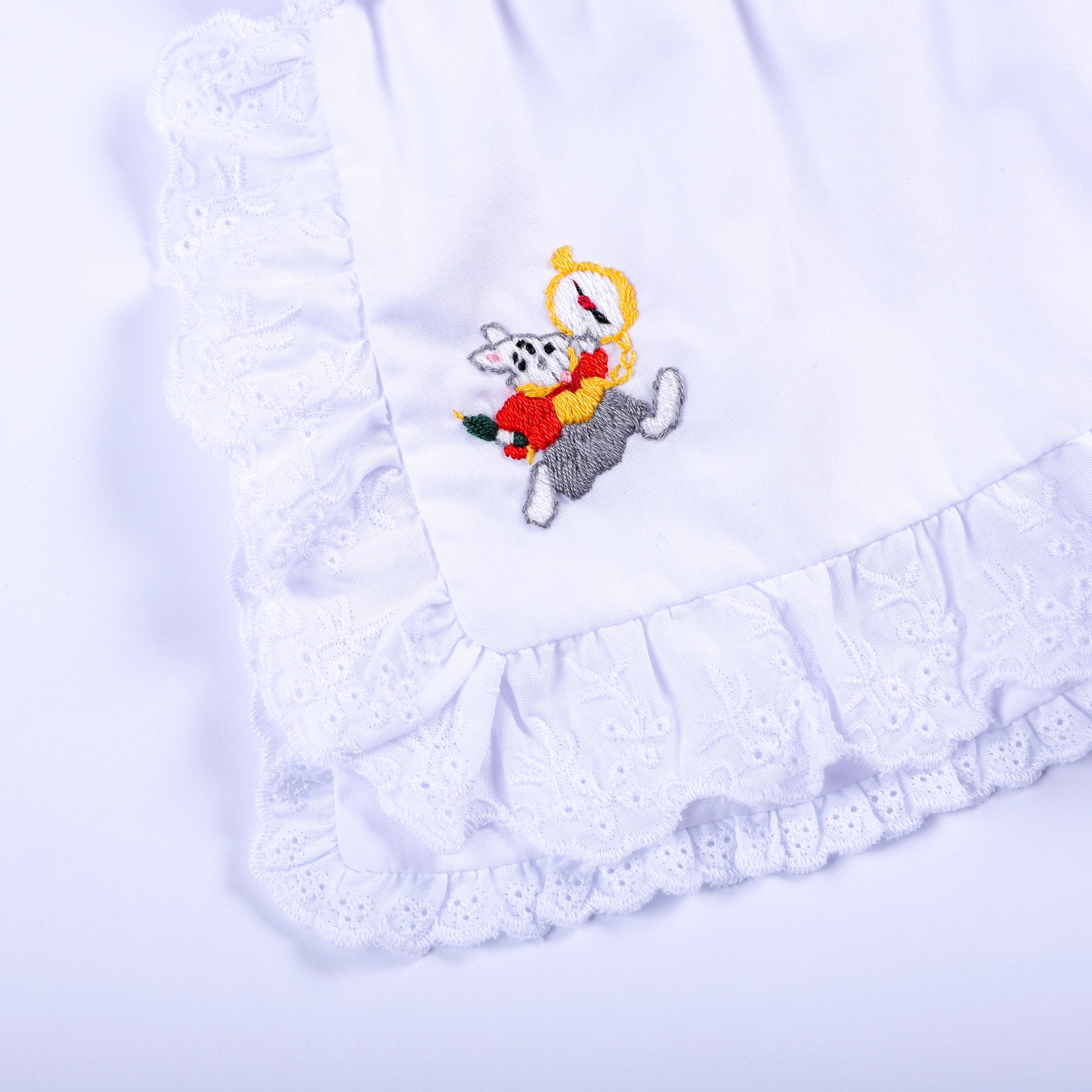 Close-up view of white ruffled apron featuring hand embroidered white rabbit character with pocket watch.
